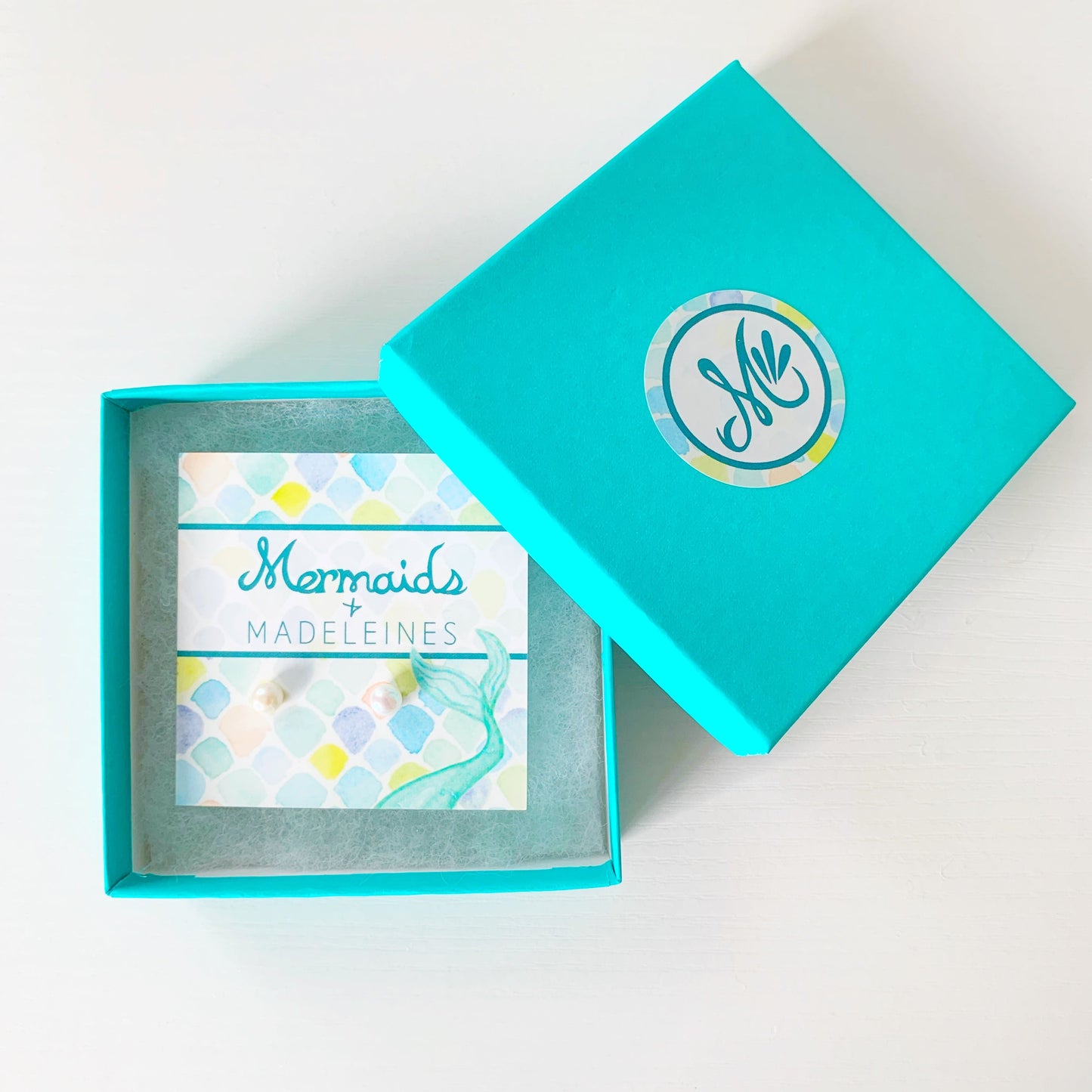 the pearlfect day stud earrings by mermaids and madeleines are available in 3 sizes. this is a photograph of the mini pair 5mm freshwater button pearl earrings with sterling silver findings carded and in a teal gift box. This is photographed on a white surface