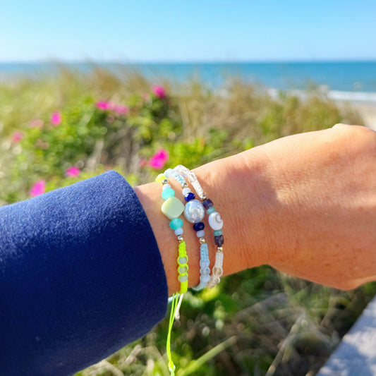 Hand wearing multiple bracelets with a scenic background of ocean and sky.