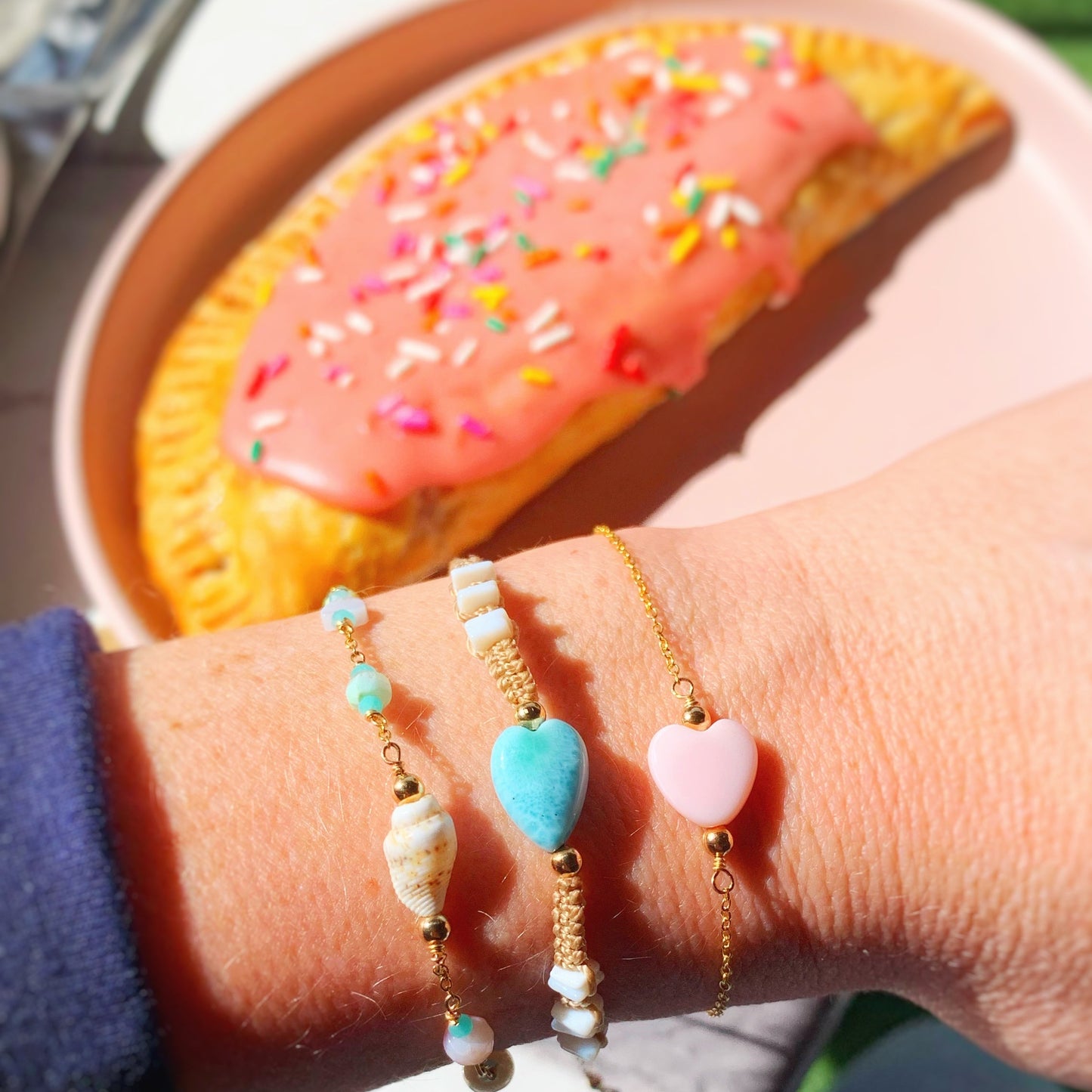 Hand wearing colorful beaded bracelets with a pastries in the background