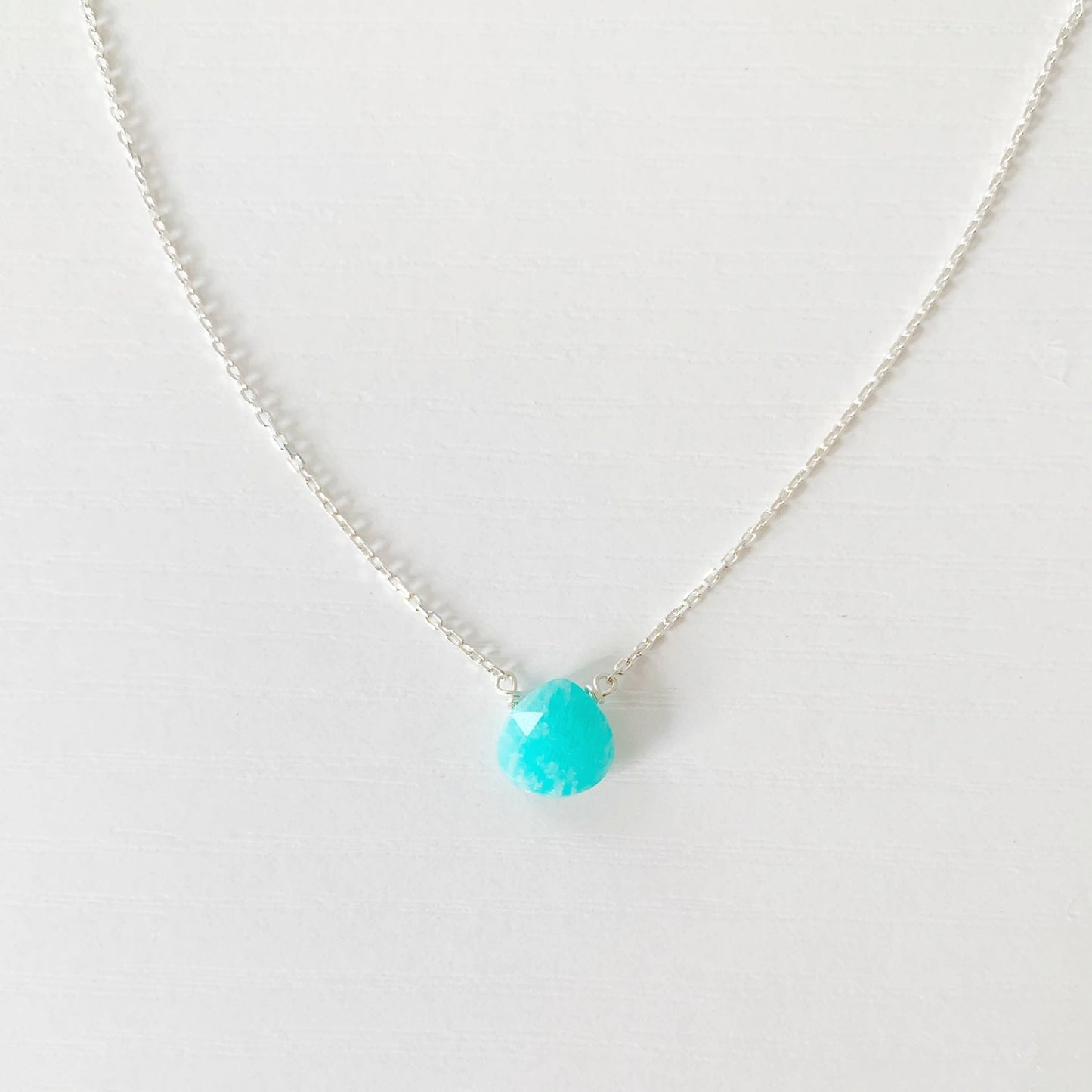 the captiva necklace by mermaids and madeleines is a dainty drop necklace featuring a small, faceted, bright teal amazonite briolette, on 17" sterling silver lightweight chain. This necklace is photographed close up on a white surface
