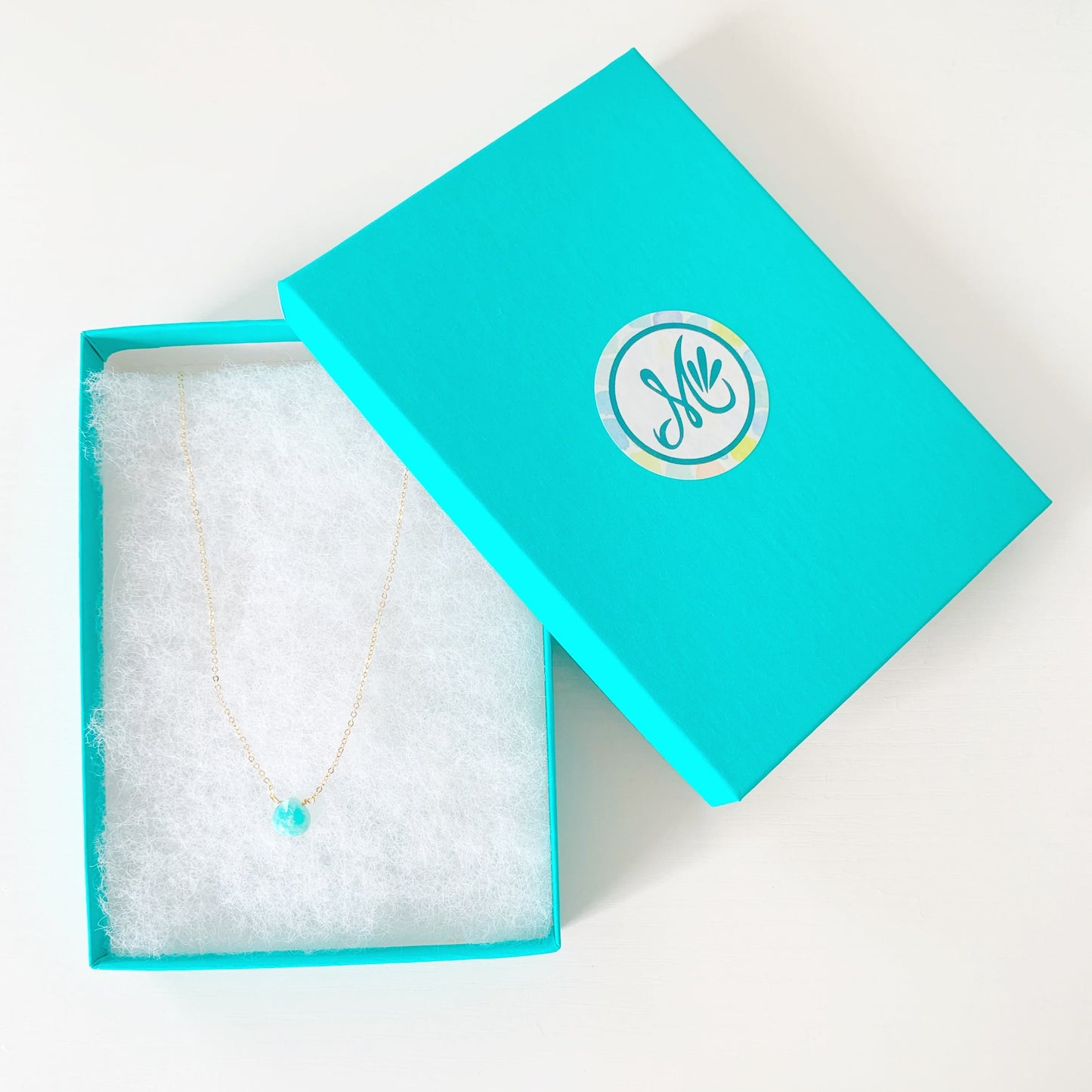 the captiva necklace by mermaids and madeleines is a dainty drop style necklace with a small, faceted bright teal amazonite briolette on 17" 14k gold filled lightweight chain. this necklace is placed in a teal gift box and photographed on a white surface