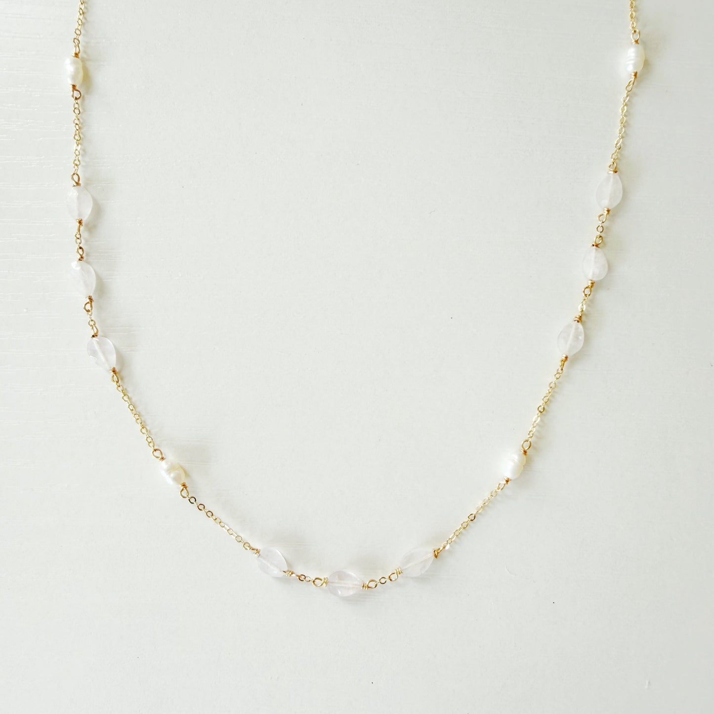 dainty 14k gold filled chain necklace with white irregular pearls and light pink kunzite beads spaced out on the necklace. necklace is photographed on a white surface