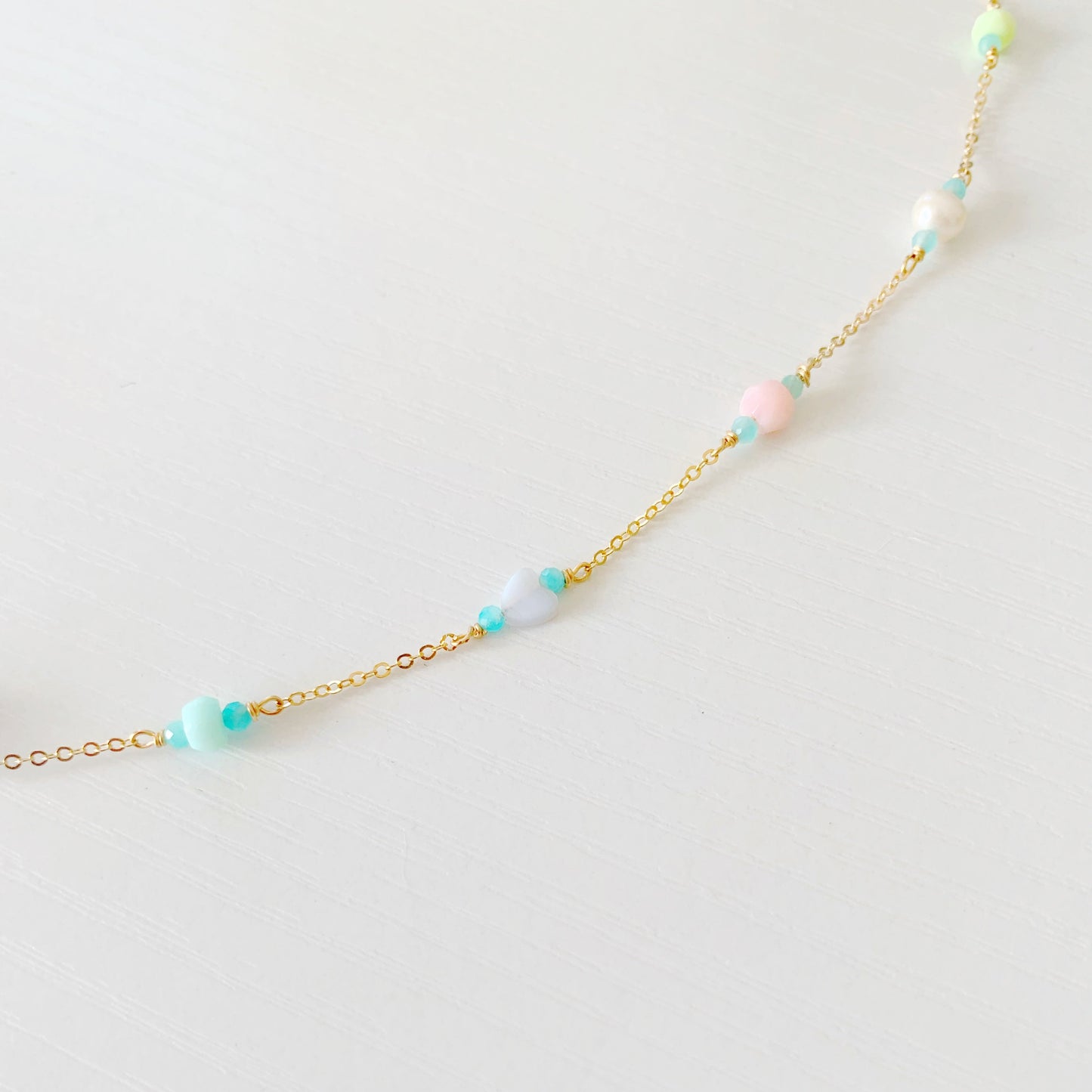 the island hopper necklace by mermaids and madeleines is a station style necklace with a shell at the center and semiprecious beads going up the 14k gold filled chain. this is a detail shot of the necklace that shows one side of the semiprecious beads on a white surface