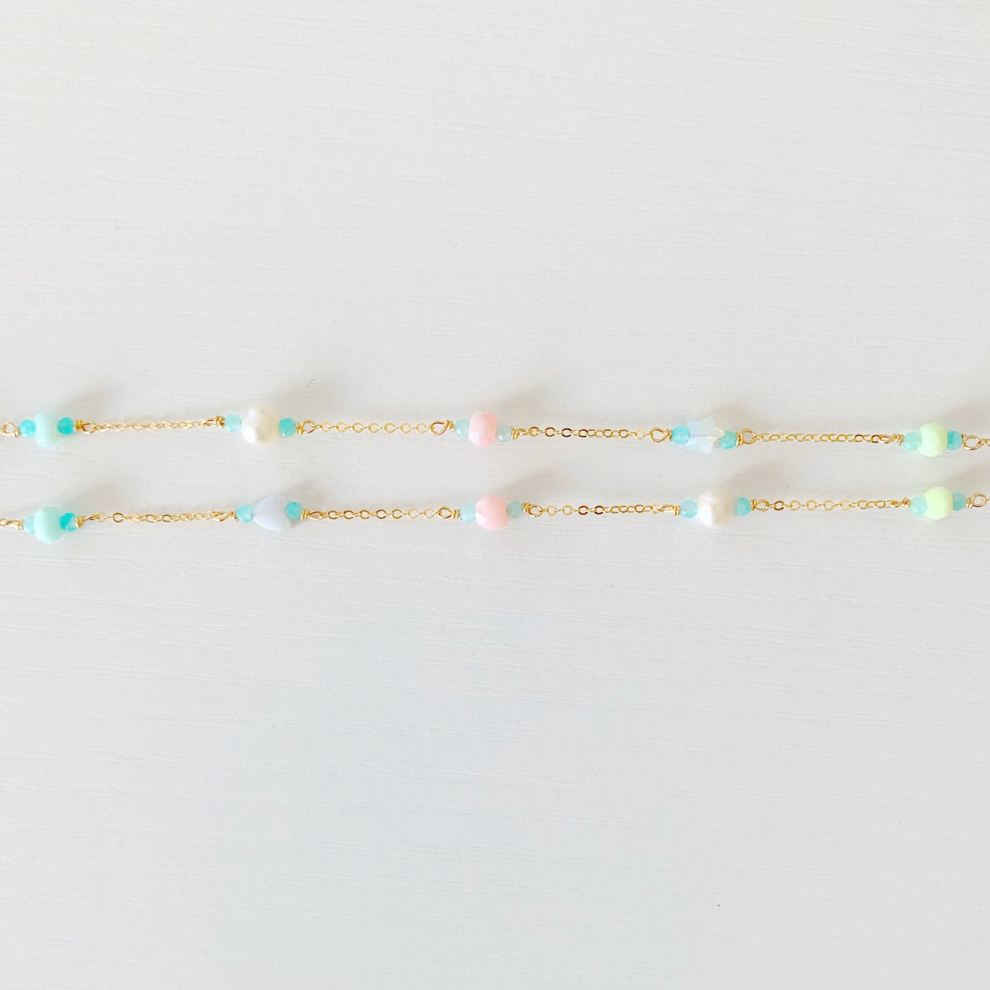 the island hopper necklace by mermaids and madeleines is a station style necklace with a shell at the center and semiprecious beads going up the 14k gold filled chain. this is a photograph of the two sides of the necklace with the semiprecious beads on a white surface