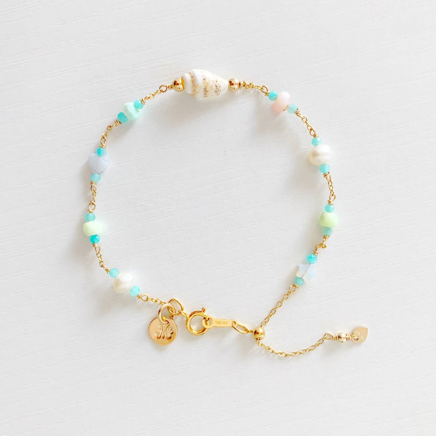 the island hopper adjustable bracelet by mermaids and madeleines is a station style bracelet with a shell at the center and semiprecious beads going up the sides of the 14k gold filled chain. this bracelet is photographed from the top down on a white surface