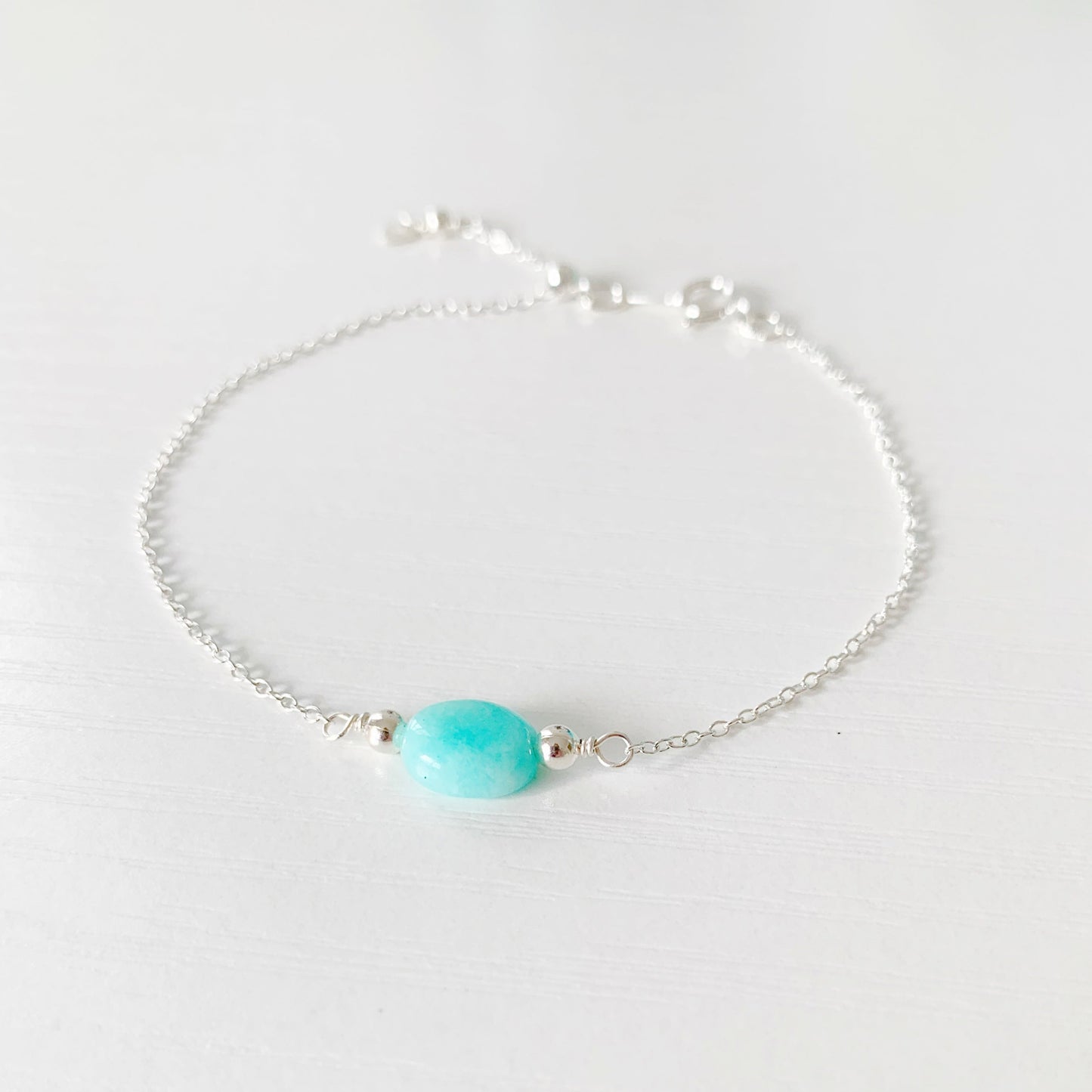 the laguna bracelet by mermaids and madeleines is a chain based bracelet with an aqua amazonite oval bead at the center and a sterling silver slide bead at the clasp. this bracelet is photographed flat on a white surface