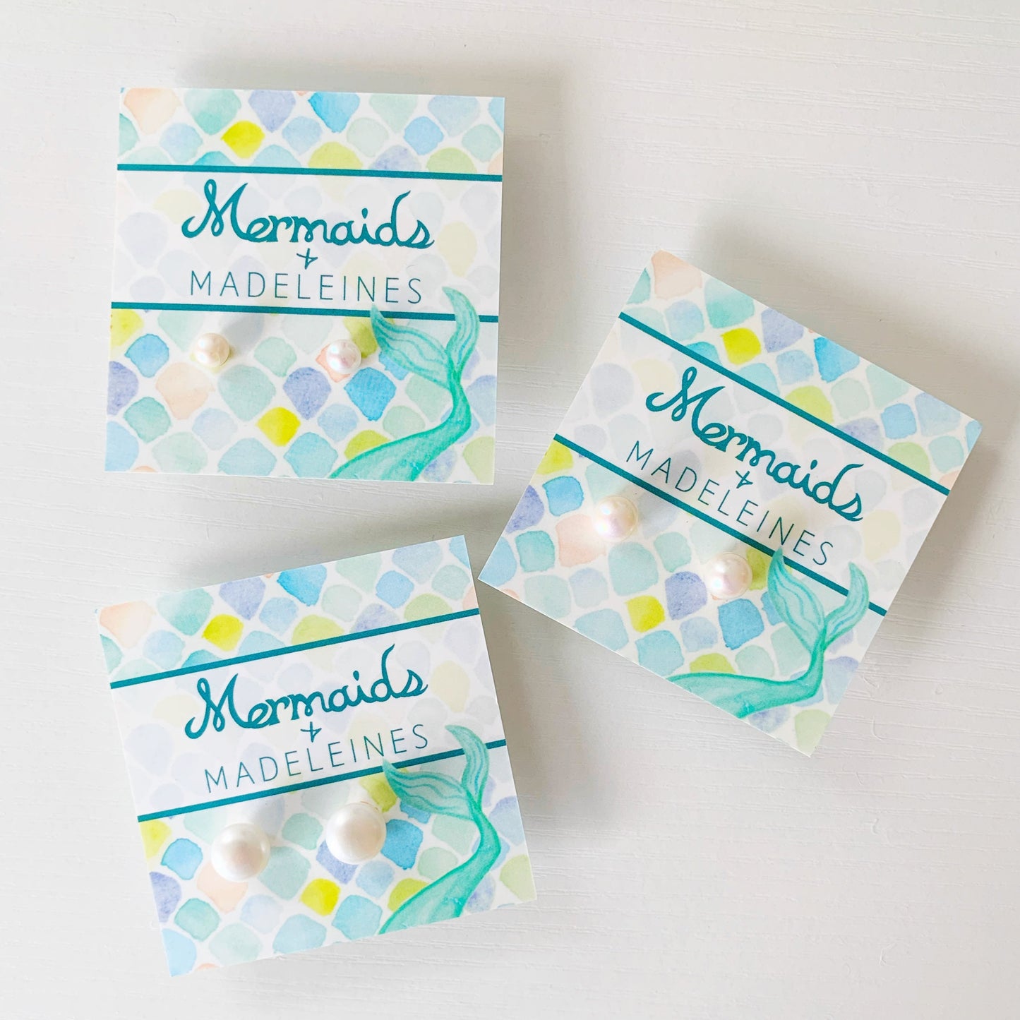 The pearlfect day pearl stud earrings by mermaids and madeleines are available in 3 sizes. The earrings are created with freshwater button pearls and sterling silver findings. This is a photograph of the 3 sizes on branded cards next to each other on a white surface
