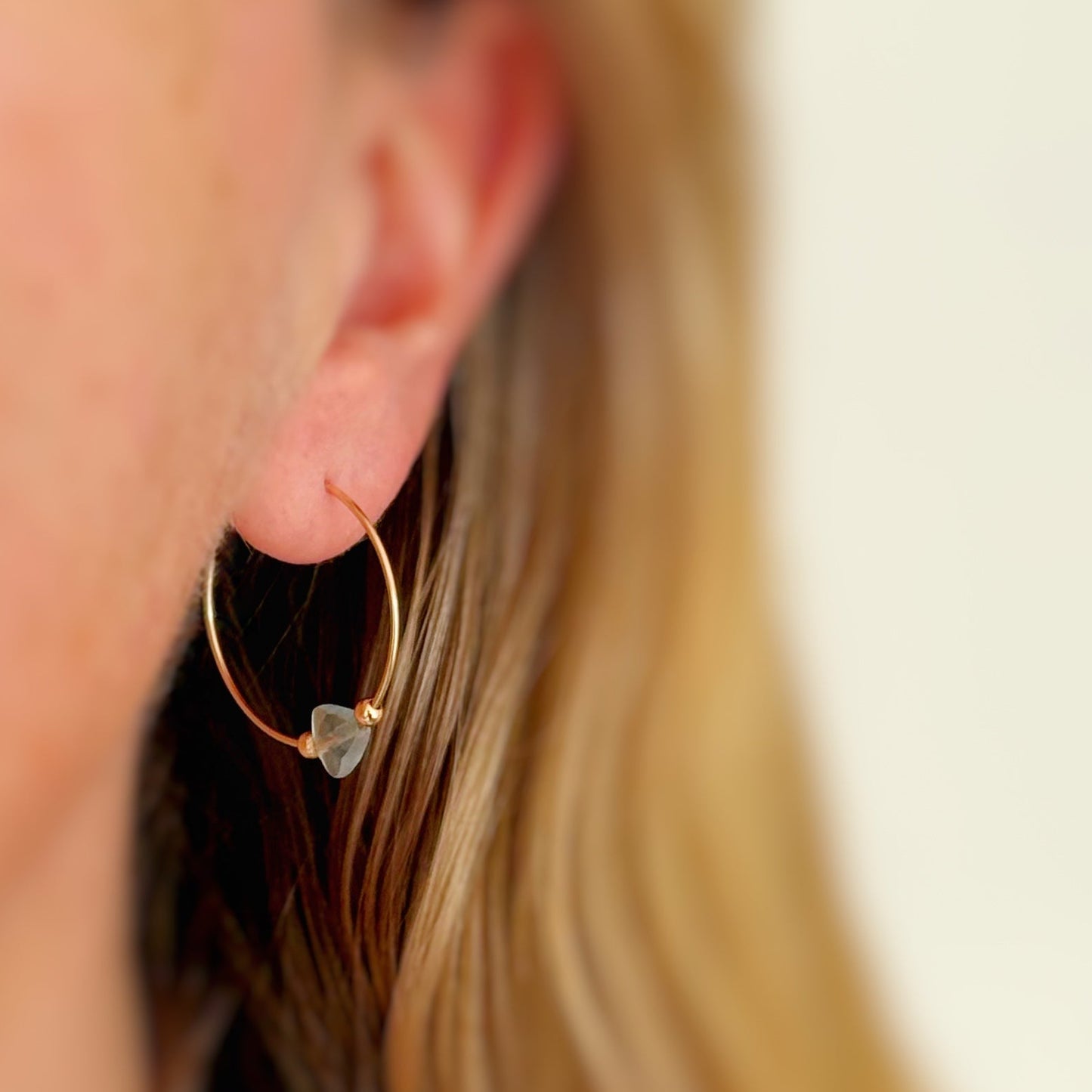 Close-up of a gold hoop earring with a triangle shaped bead worn by a person.