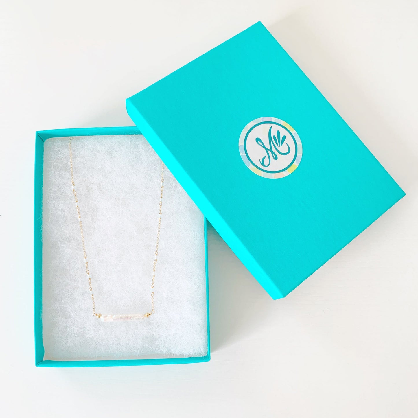 the truro necklace by mermaids and madeleines is a 14k gold filled necklace with a freshwater pearl center and aquamarine beads going up the sides. this necklace is photographed in a teal gift box on a white surface