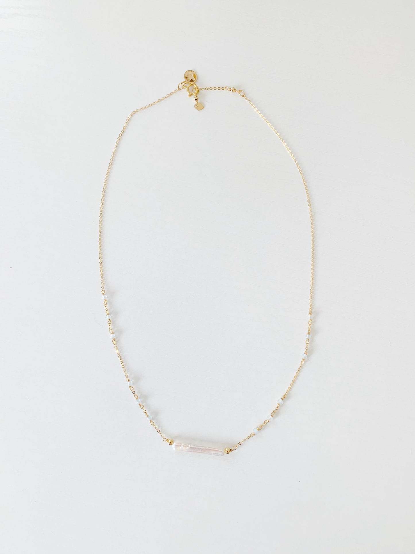 the truro necklace by mermaid and madeleines is a 14k gold filled chain necklace with a freshwater pearl at the center and aquamarine beads going up the sides. this is a photograph of the full length of the necklace on a white surface