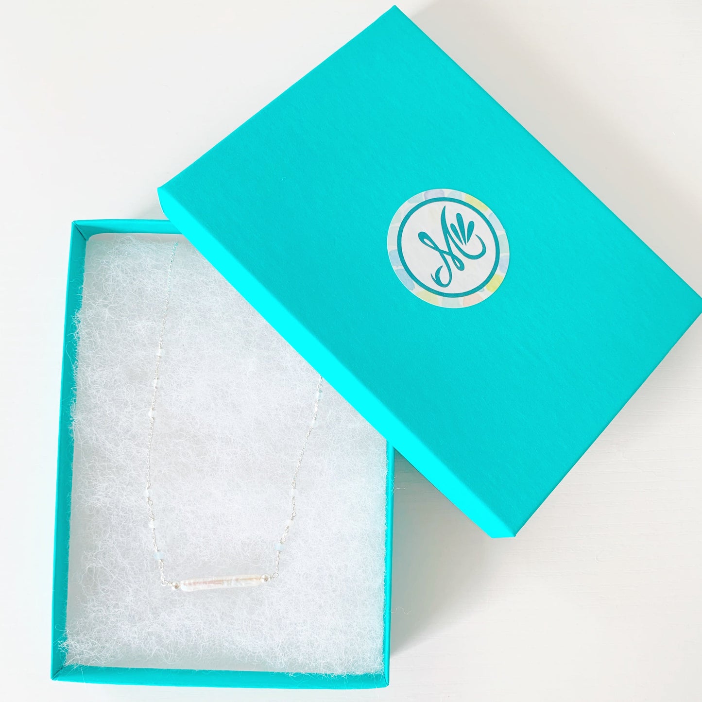 the truro necklace by mermaids and madeleines is a sterling silver chain necklace with a freshwater stick pearl at the center and aquamarine beads going up the sides. this necklace photographed in a teal gift box on a white surface