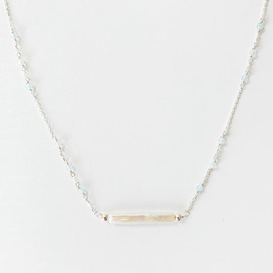 The Truro Necklace by Mermaids and Madeleines features a freshwater stick pearl at the center like a horizontal bar necklace with tiny microfaceted aquamarine beads going up the chain on either side. the chain and findings are sterling silver. this necklace is photographed on a white surface
