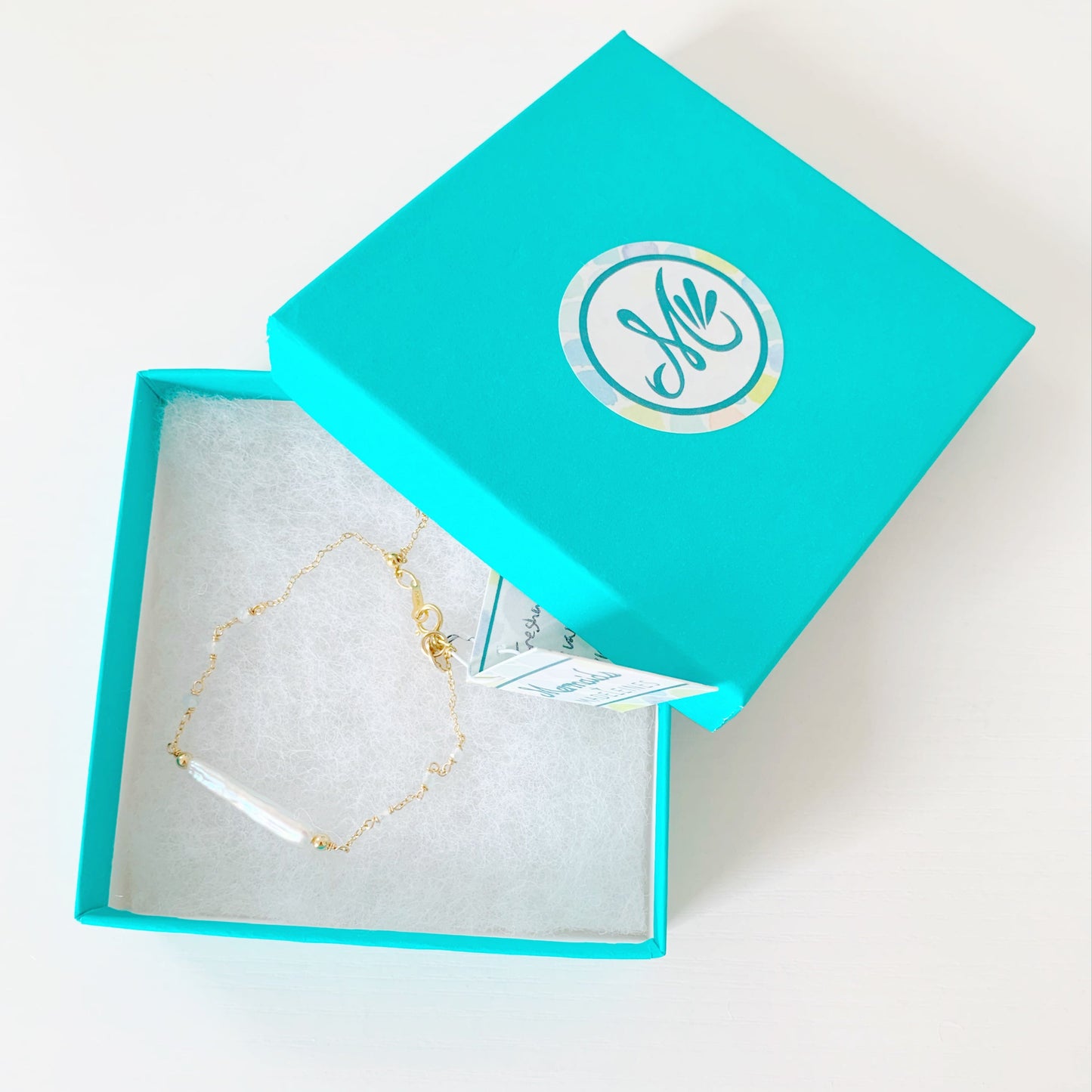 the truro bracelet by mermaids and madeleines is a 14k gold filled chain bracelet with a freshwater stick pearl at the center and with aquamarine faceted beads going down the sides with a slide bead at the clasp to make it adjustable. this bracelet is photographed in a teal gift box on a white surface