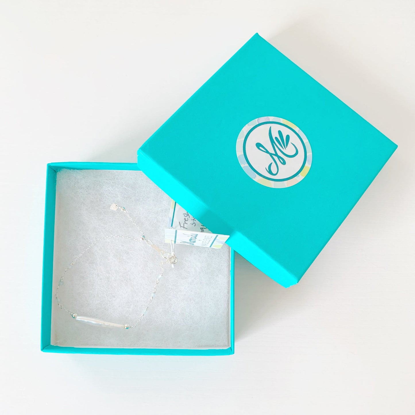 the truro bracelet by mermaid and madeleines is an adjustable chain style bracelet with freshwater stick pearl at the center with small faceted aquamarine beads in stations going down the sides. This bracelet has sterling silver findings, slide bead and chain and is placed in a teal gift box. All items are photographed on a white surface in a top down view