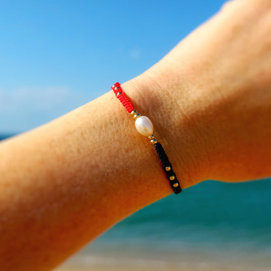 Hand wearing a bracelet with red and black beads against a beach background