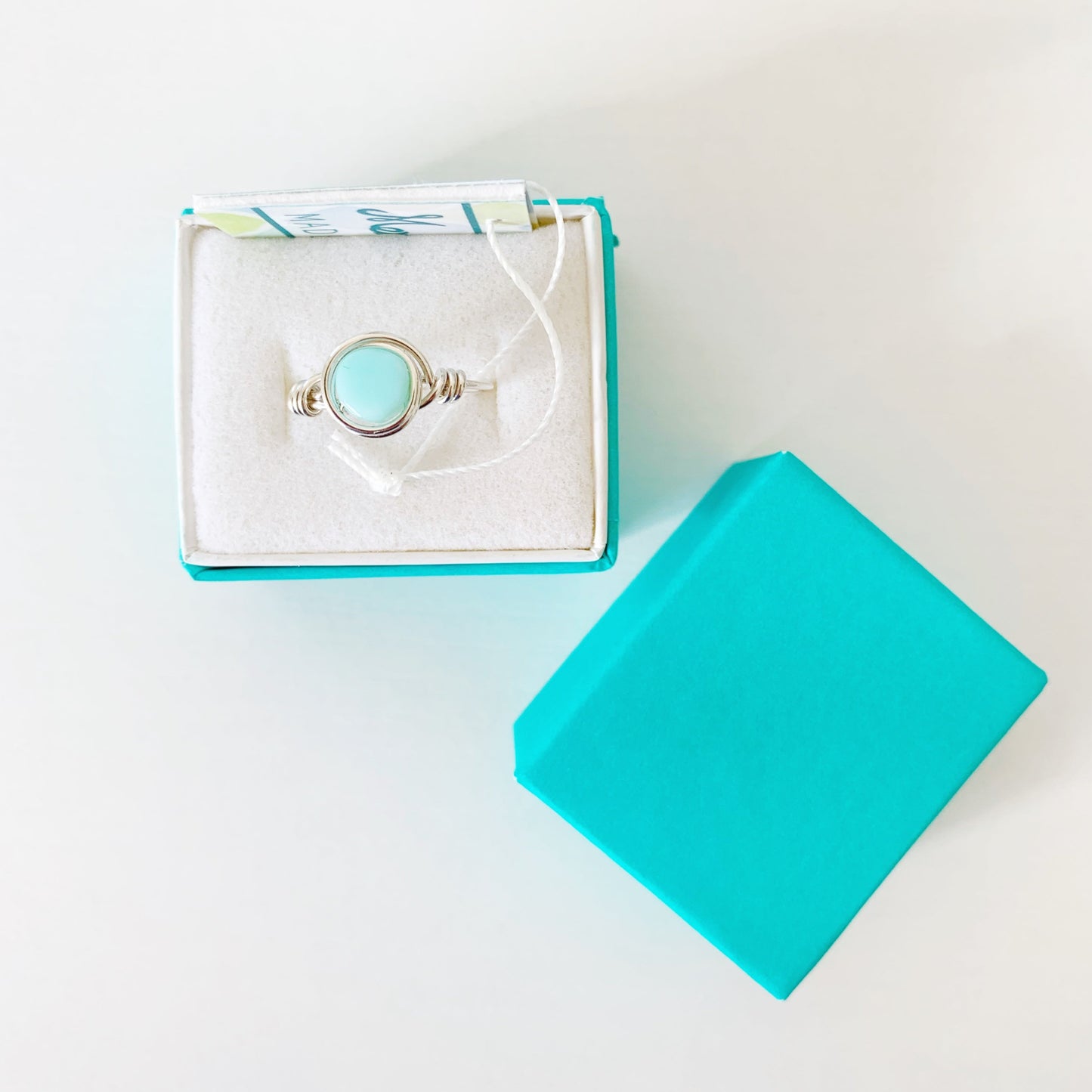the island hopper ring by mermaids and madeleines is a sterling silver wire-wrapped style ring with a Peruvian opal coin bead at the center. this ring is photographed from the top down in a teal gift box on a white surface