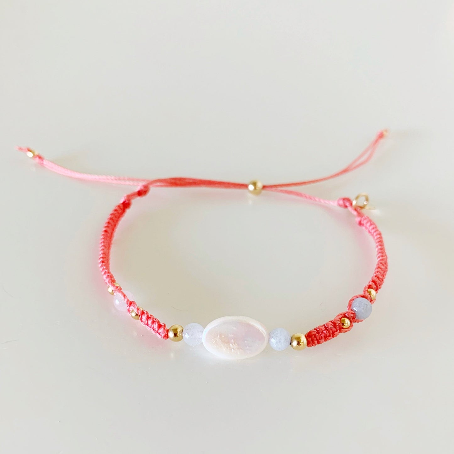 the kinda crabby bracelet by mermaids and madeleines is an adjustable macrame style bracelet created with terra cotta cord with a freshwater oval pearl center and 4mm aquamarine beads on either side. this bracelet is photographed from the front on a white surface
