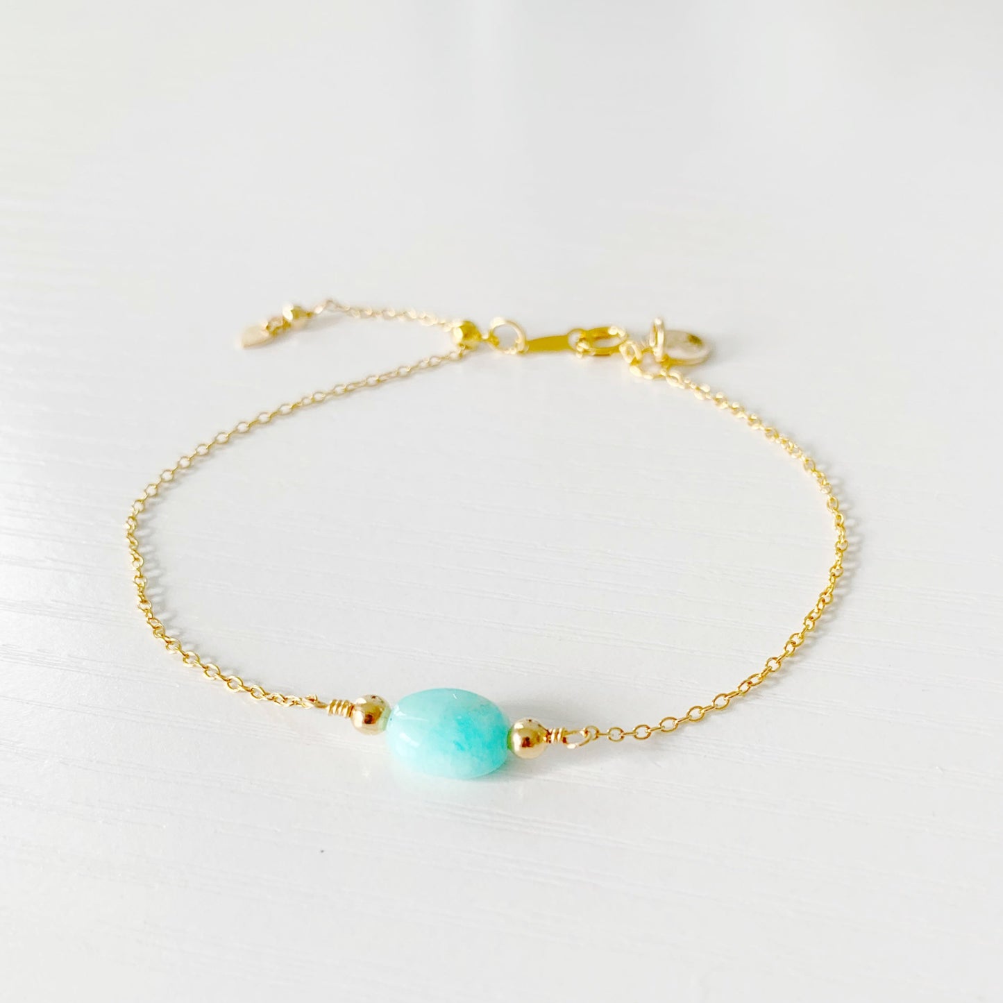 the laguna bracelet by mermaids and madeleines is a 14k gold filled chain style bracelet with an aqua oval amazonite at the center. There's a slide bead near the clasp that makes the bracelet adjustable. this bracelet is photographed from the front on a white surface