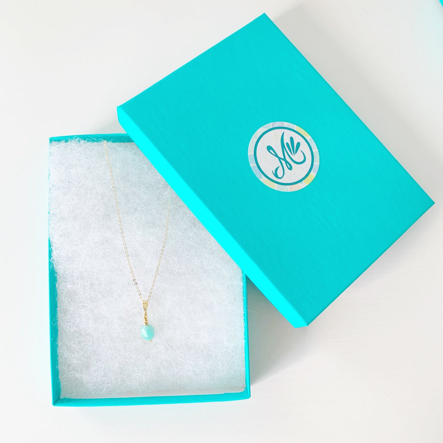 the mermaids and madeleines laguna necklace is created in a pendant style with an amazonite oval on 14k gold filled findings and chain. this necklace is photographed in a teal gift box on a white surface