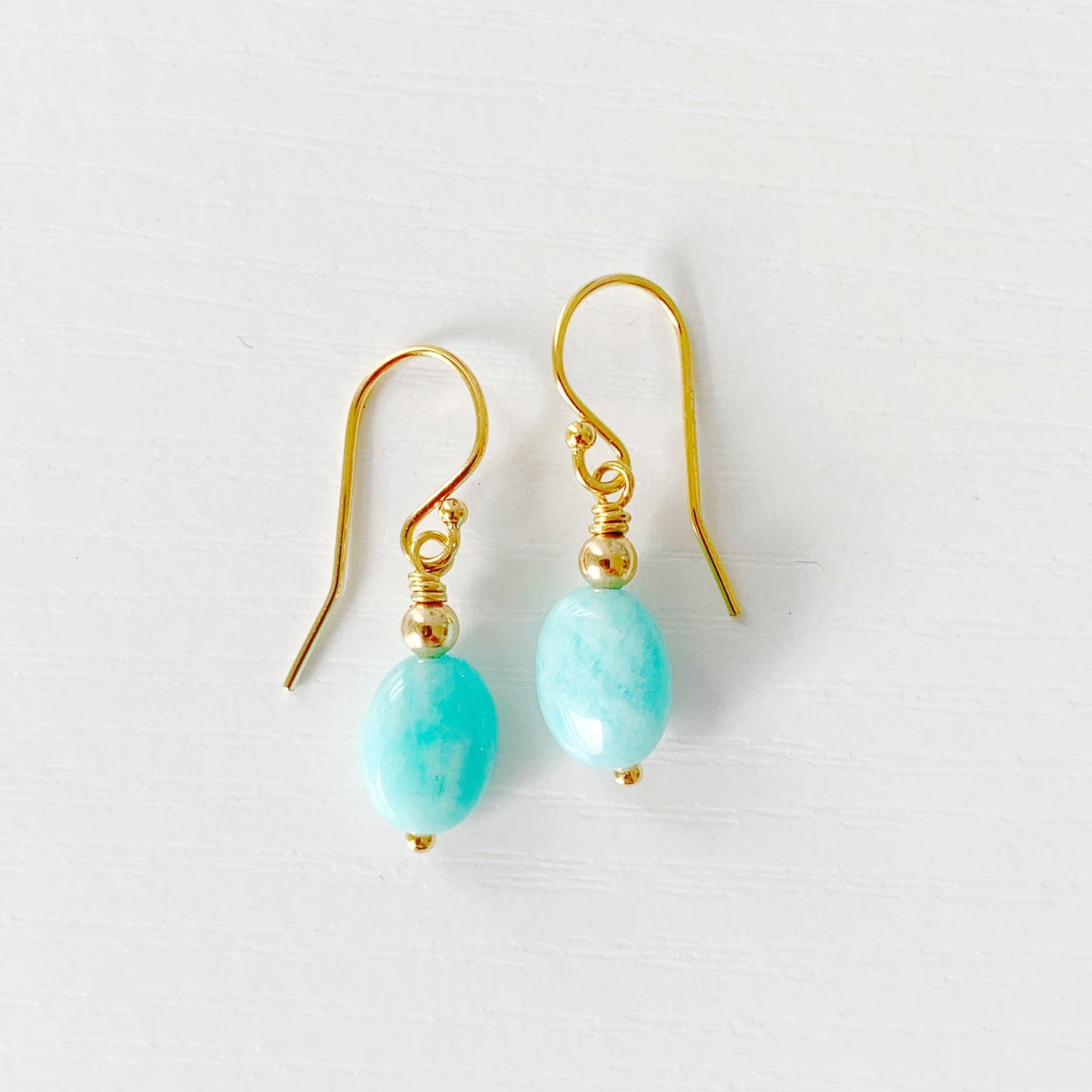 the laguna earrings by mermaids and madeleines are simple drop earrings with aqua drop amazonite beads hanging from 14k gold filled findings and ear wires. this pair is photographed on a white surface