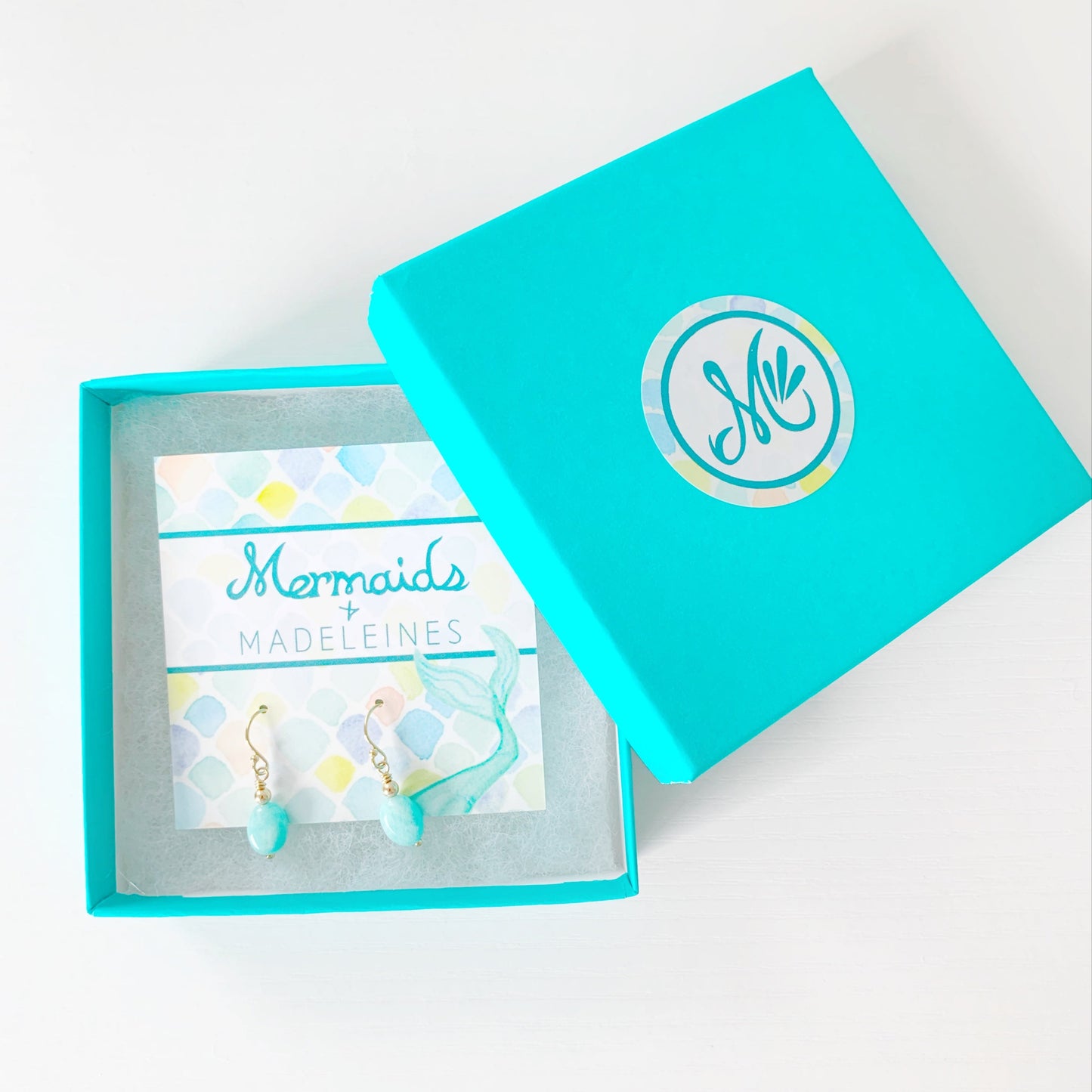 the laguna earrings by mermaids and madeleines are aqua, oval amazonite beads dropped from 14k gold filled findings and ear wires. this pair is carded and placed in a teal gift box, photographed on a white surface