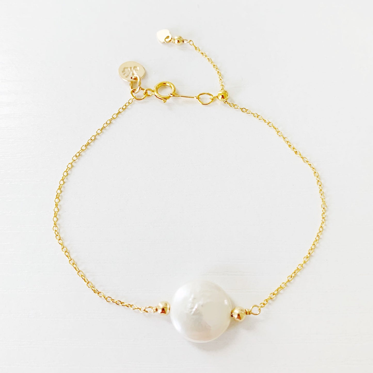 mermaids and madeleines newport adjustable bracelet is made with a fresheater coin pearl on the center with 14k gold filled chain and findings. theres a slide bead near the clasp to tighten the bracelet. this bracelet is photographed from a top down view on a white surface