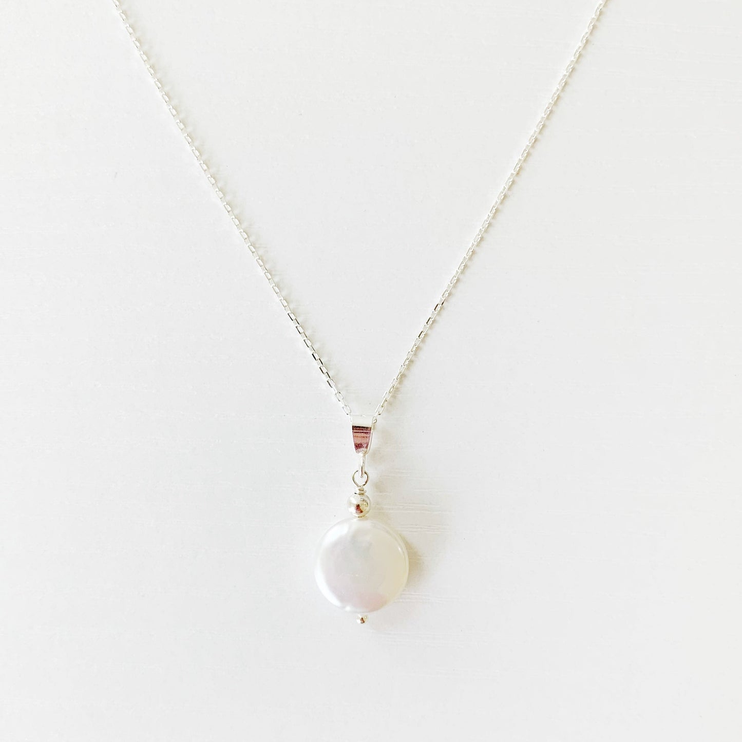 the newport necklace by mermaids and madeleines is a freshwater coin pearl suspended from a sterling silver chain and findings. this necklace is photographed on a white surface