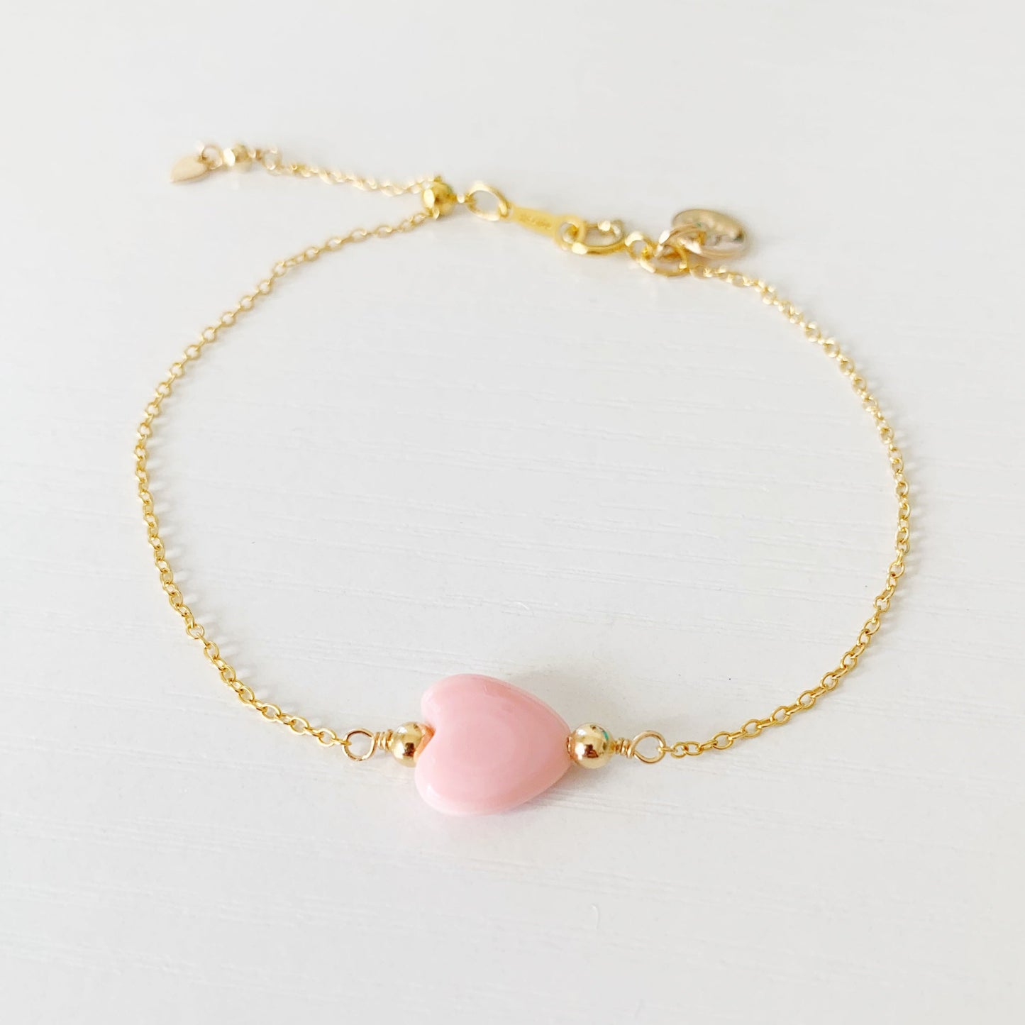 the pink posy adjustable bracelet by mermaids and madeleines is a chain style bracelet with a light pink, conch shell heart bead at the center. this bracelet is photographed from the front on a white surface