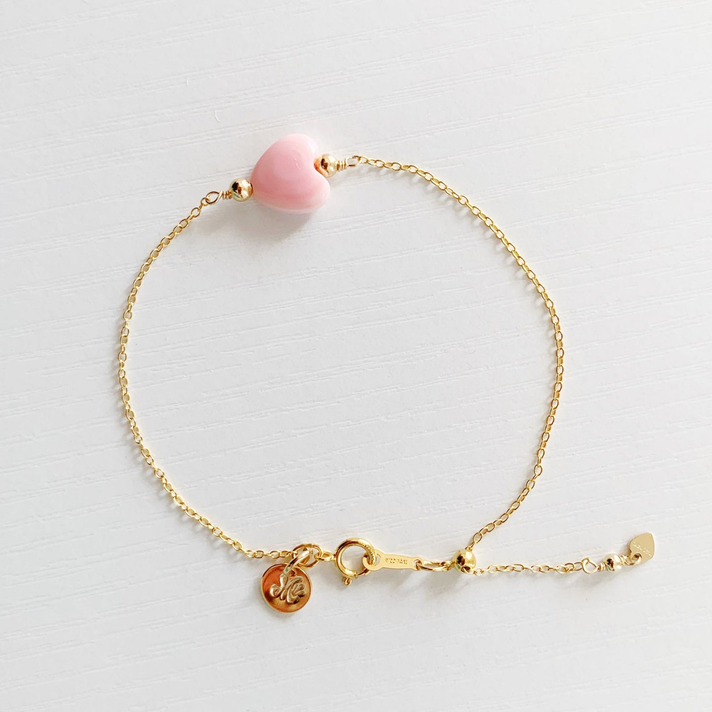 the pink posy adjustable bracelet by mermaids and madeleines is a chain style bracelet with a light pink, conch shell heart bead at the center. this bracelet is photographed from the top down on a white surface