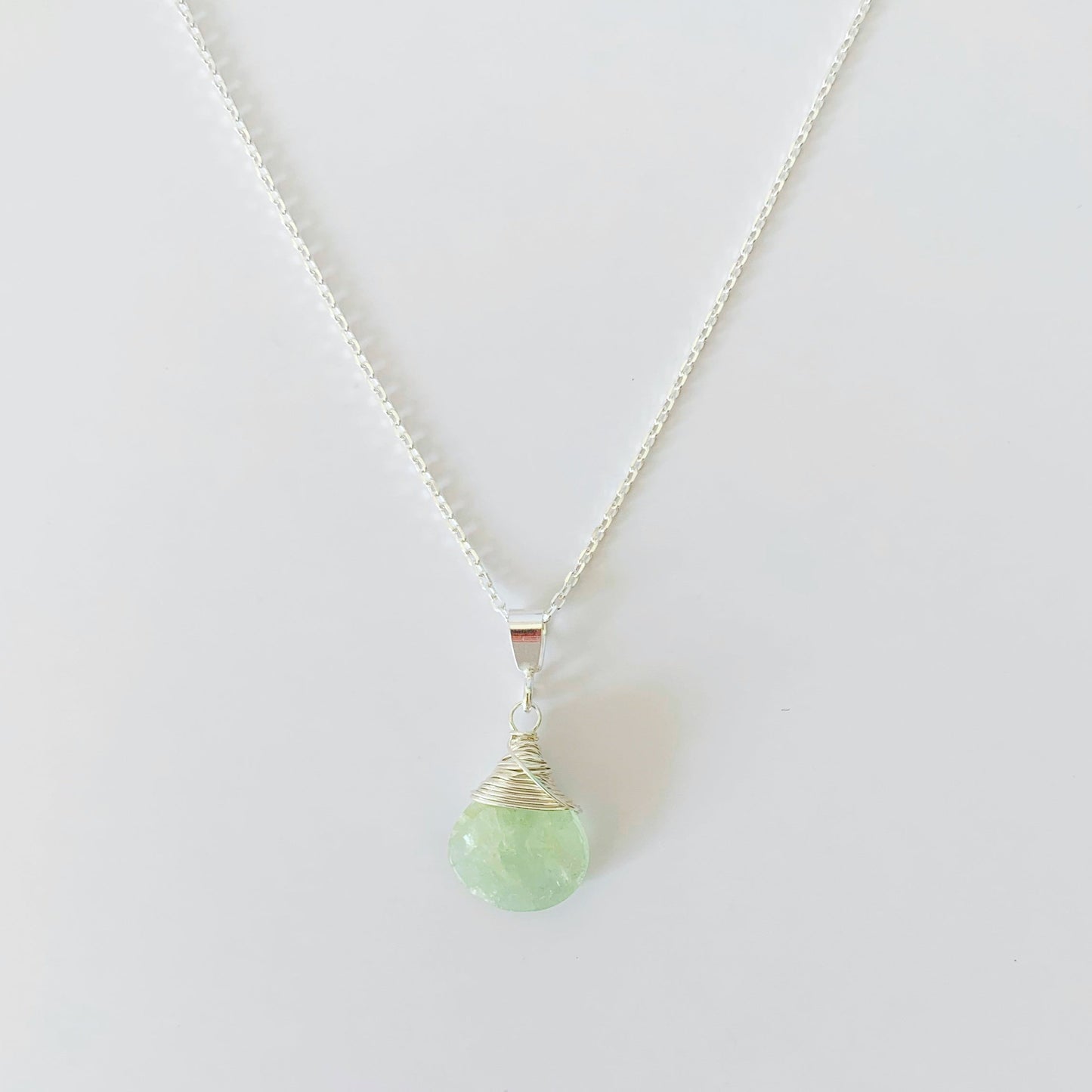 a wire wrapped aquamarine briolette with sterling silver suspended from a thin cable chain necklace. this picture is over a white surface