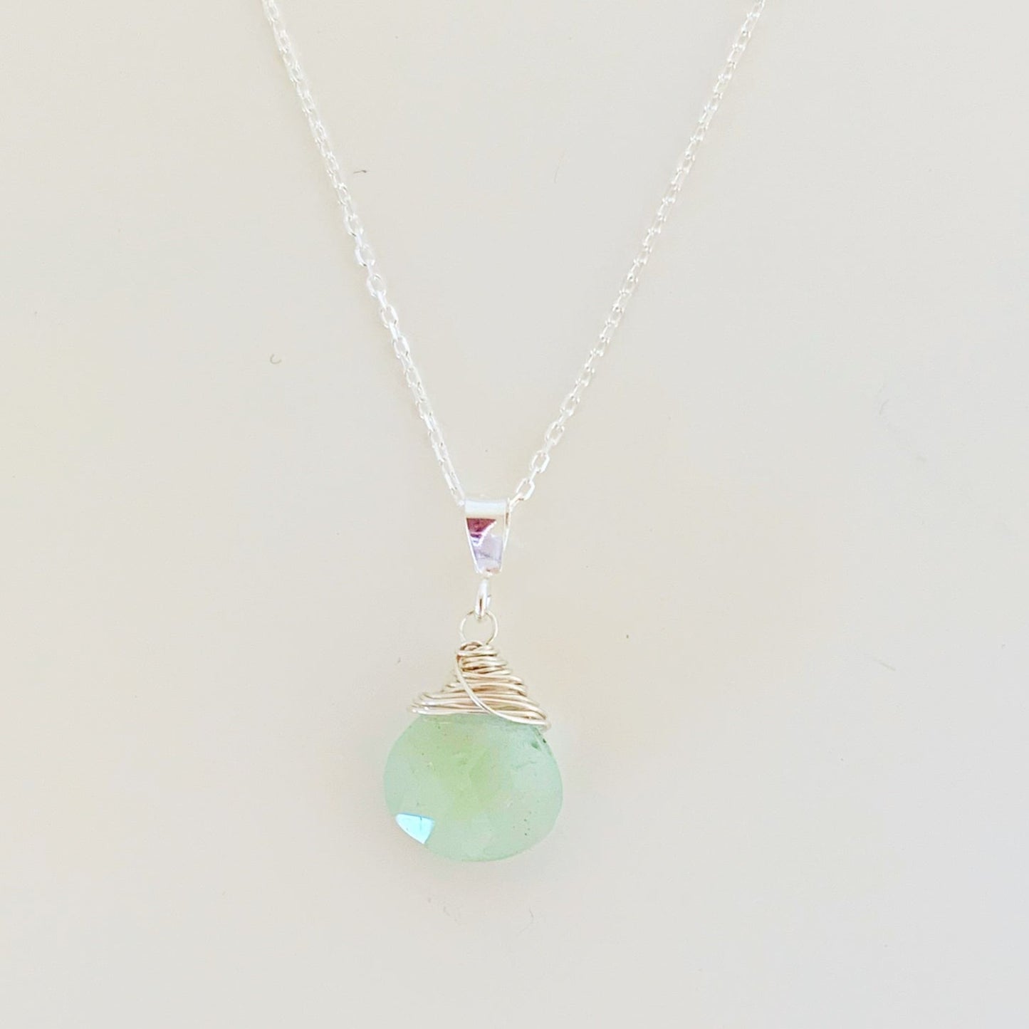 the raindrop necklace by mermaids and madeleines is a pendant design created with a faceted aquamarine briolette wire wrapped with sterling silver and hanging from sterling silver chain. photographed on a white surface