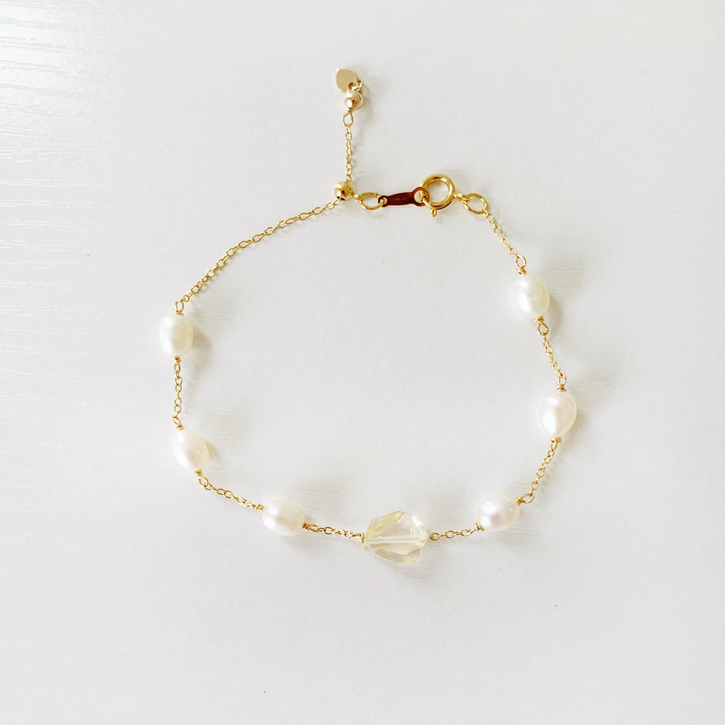 The sun and snow bracelet by mermaids and madeleines is an adjustable 14k gold filled chain bracelet with a slide bead at the clasp. the bracelet features a light yellow faceted citrine gem at the center with freshwater rice shaped pearls going up the sides. this bracelet is photographed flat on a white surface with a top down view