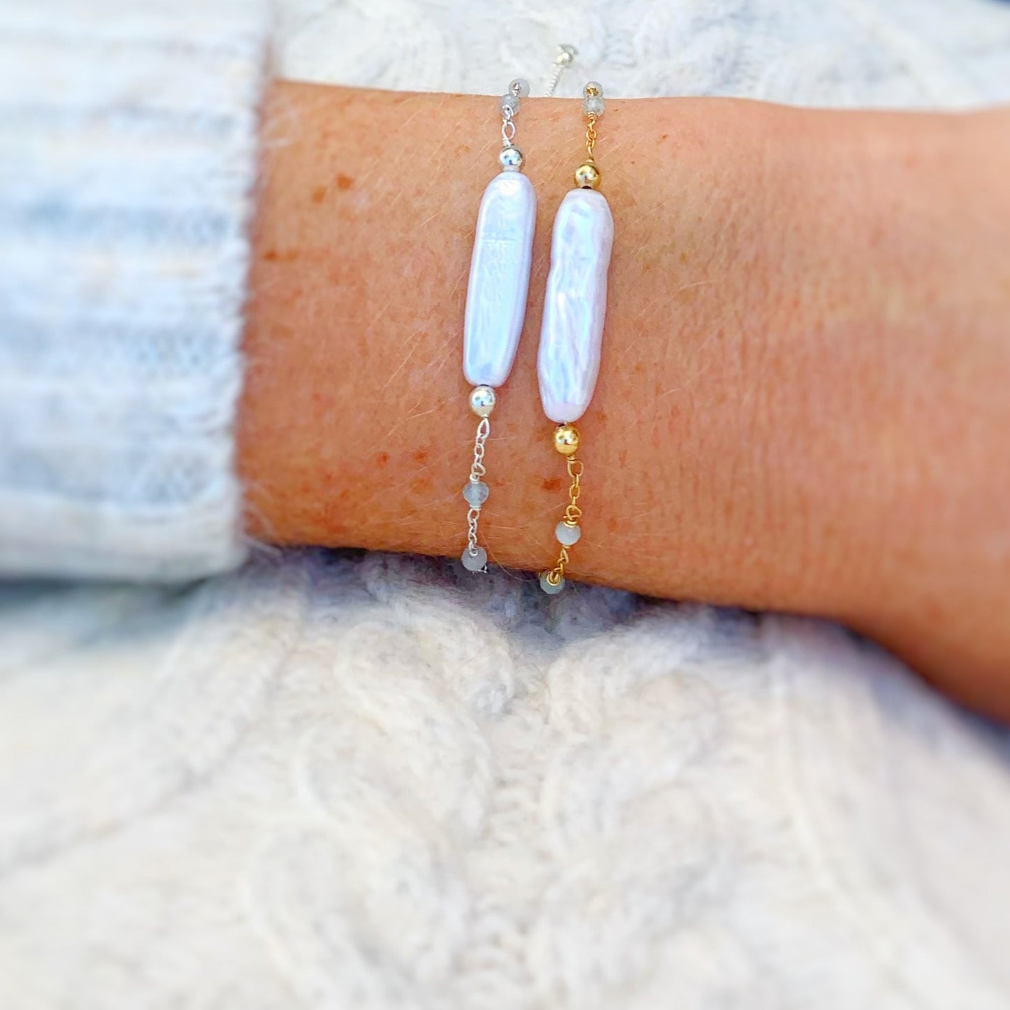 the truro adjustable bracelets by mermaids and madeleines are an adjustable chain based bracelet with a slide bead near the clasp to tighten. these bracelets have a freshwater stick pearl at the center with tiny microfaceted aquamarine beads in the chain on the sides. this image has a truro bracelet in 14k gold filled and a truro bracelet in sterling silver pictured on a wrist in a close up view with a little bit of off white sweater showing on the sleeve and in the background