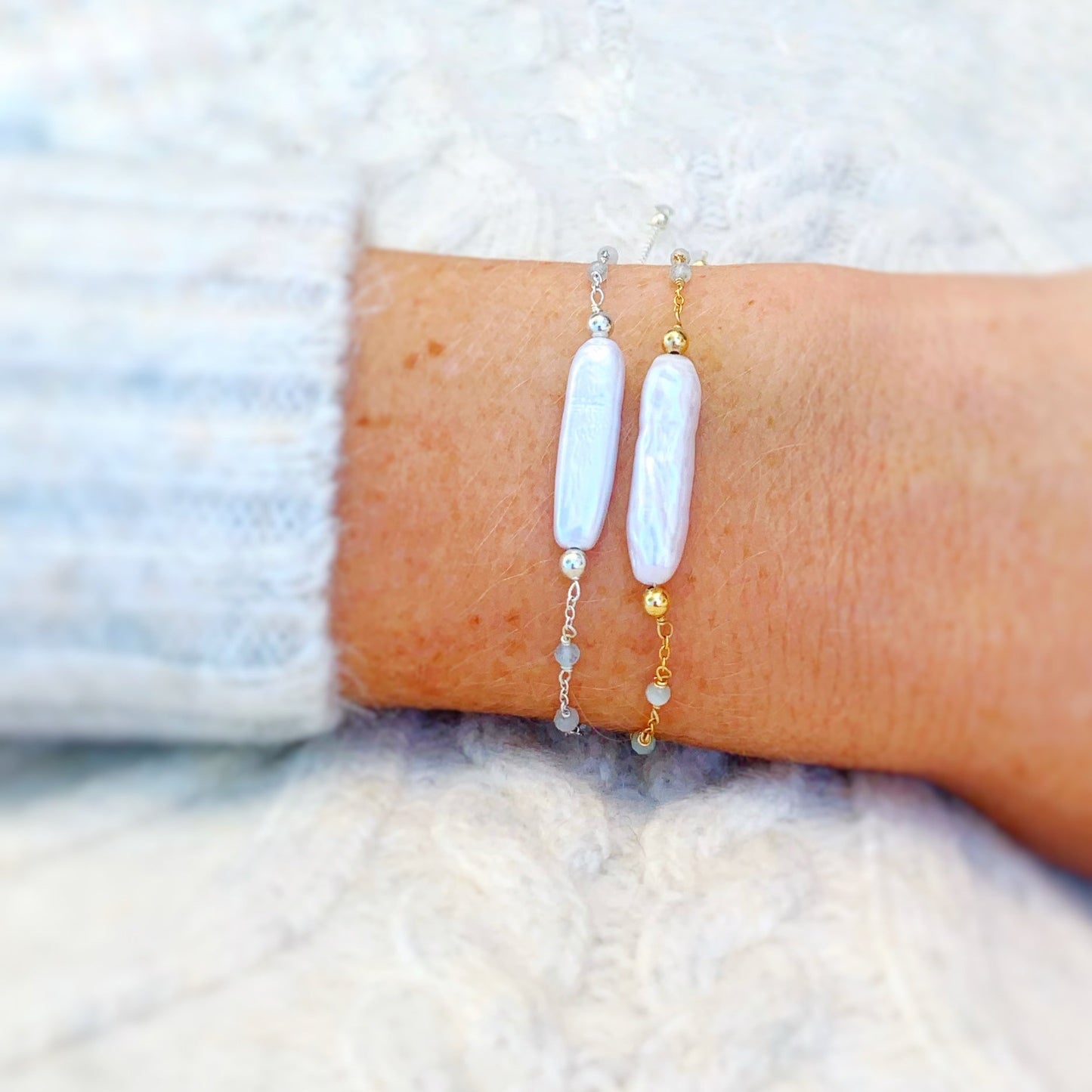 the truro adjustable bracelets by mermaids and madeleines are an adjustable chain based bracelet with a slide bead near the clasp to tighten. these bracelets have a freshwater stick pearl at the center with tiny microfaceted aquamarine beads in the chain on the sides. this image has a truro bracelet in 14k gold filled and a truro bracelet in sterling silver pictured on a wrist in a close up view with a little bit of off white sweater showing on the sleeve and in the background