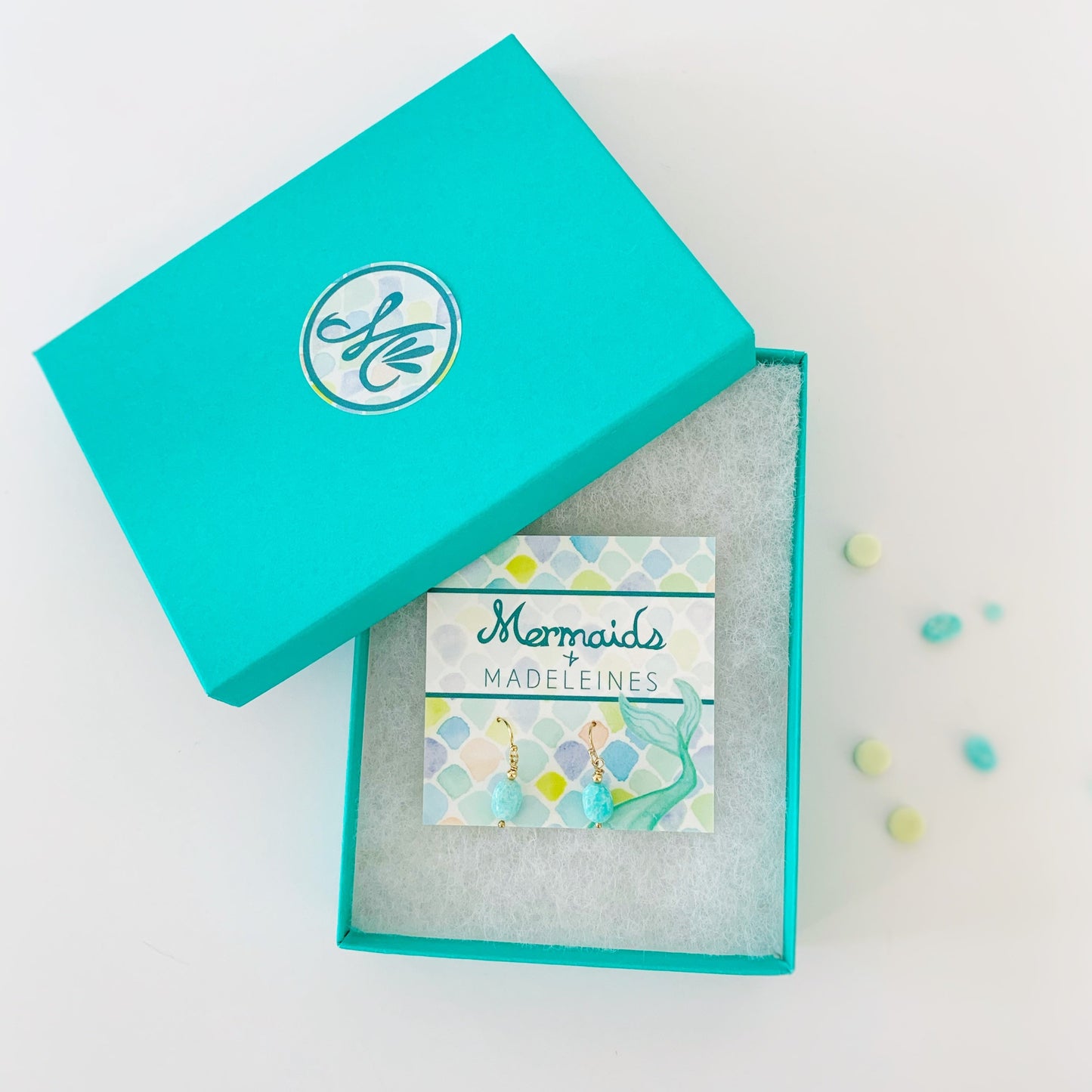 The laguna earrings in 14k gold filled. The earrings are created with 14k gold filled beads and findings and bright aqua oval shaped amazonite beads. This pair is pictured on a mermaids and madeleines card in a cotton lined teal gift box and photographed on a white background