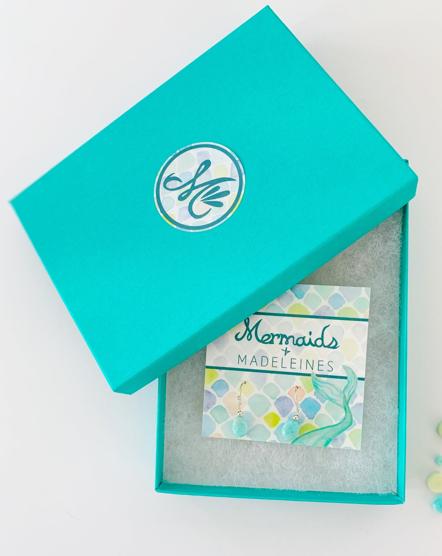 The Laguna earrings in sterling silver. This pair of laguna earrings is created with sterling silver beads and findings and bright aqua oval shaped beads. This pair is pictured on a mermaids and madeleines earring card in a cotton lined teal gift box and photographed on a white background