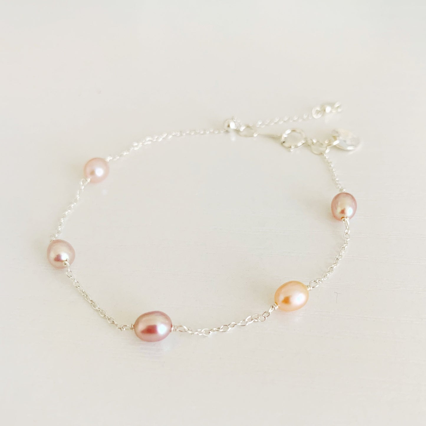 block island bracelet by mermaid and madeleines features natural pink color, small oval pearls in stations on sterling silver chain. There's a slide bead near the clasp to adjust. the bracelet is photographed on a white surface
