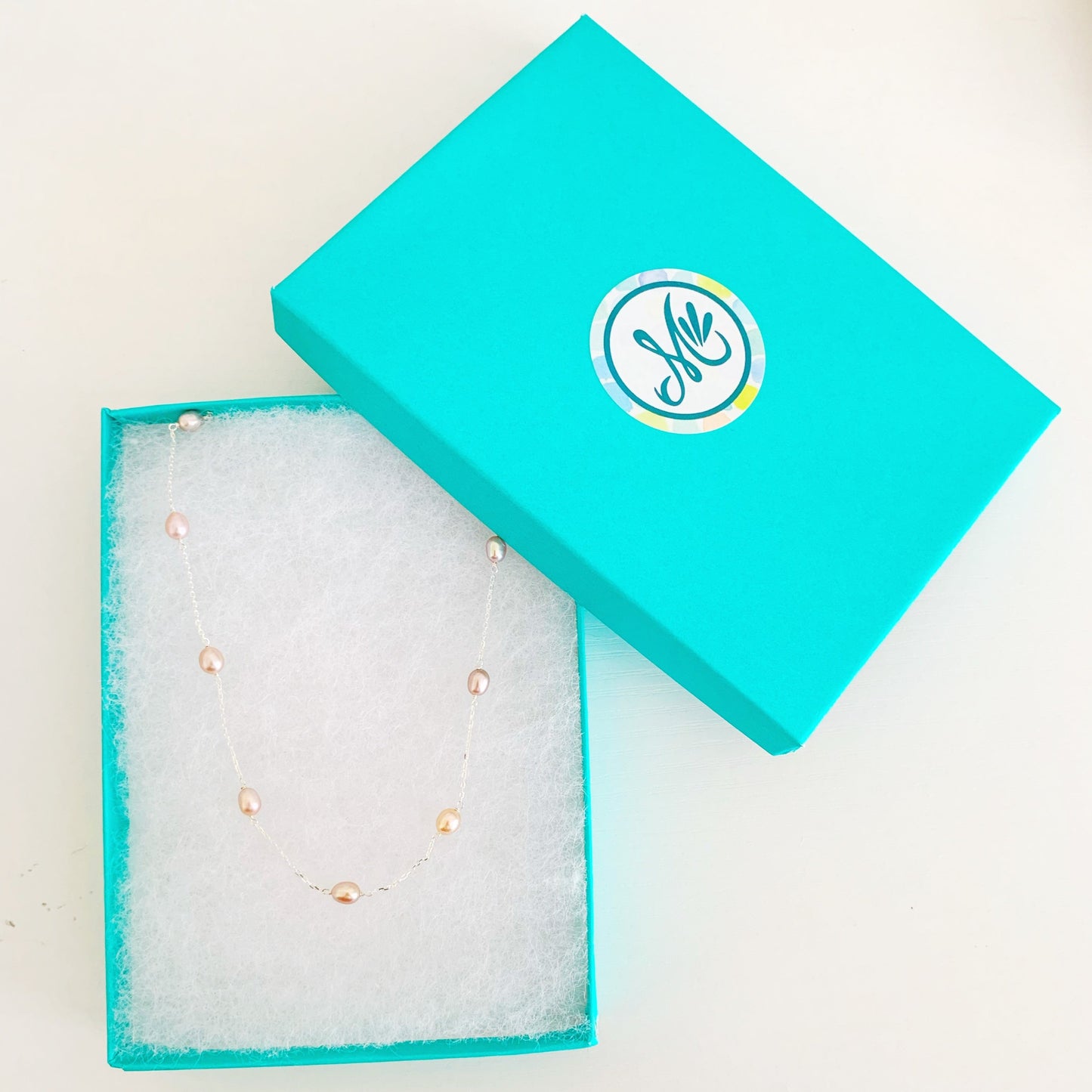 Block Island necklace by mermaids and madeleines features natural color pink freshwater pearls in stations on sterling silver chain. this necklace is photographed in a cotton lined teal gift box on a white surface