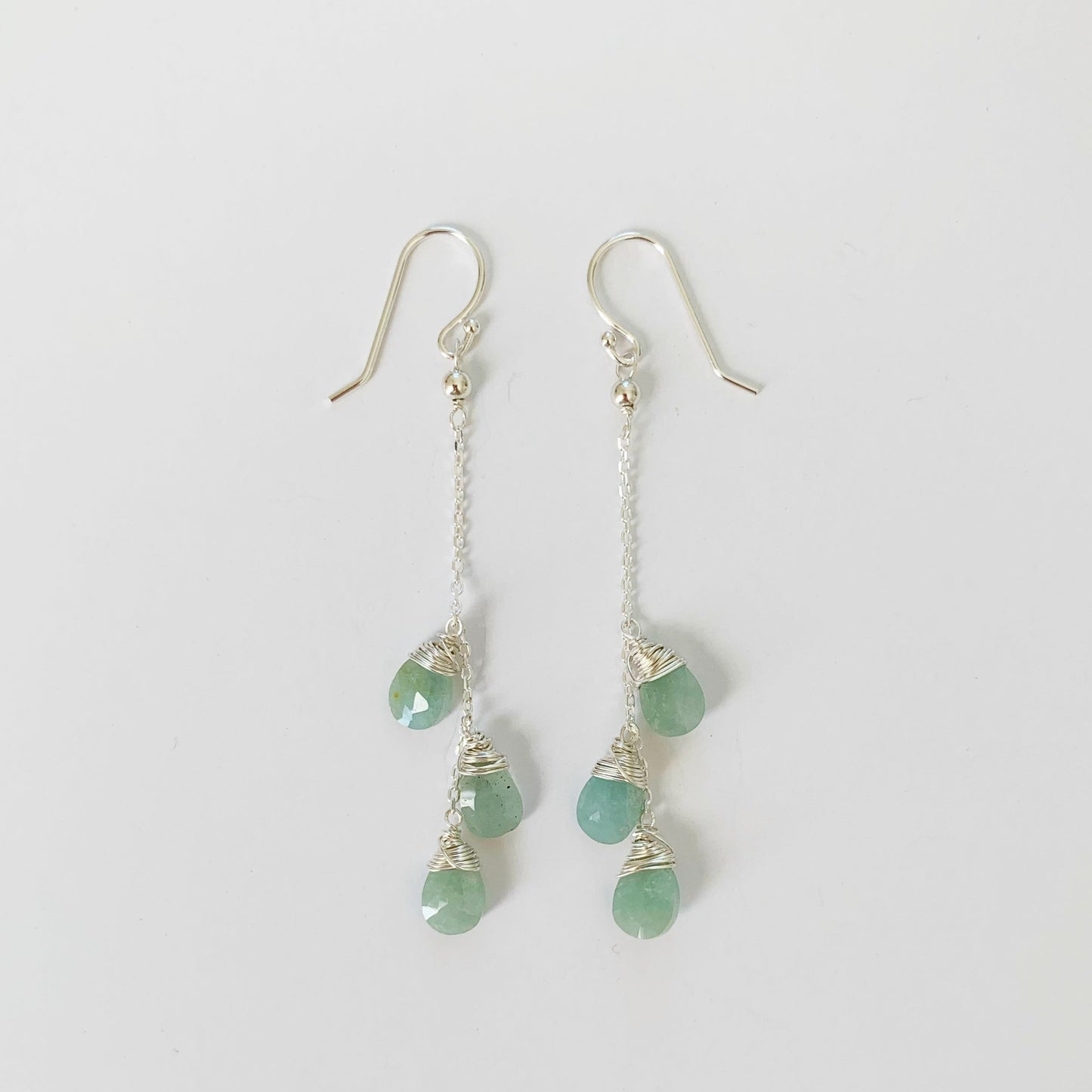 Raindrop Earrings by Mermaids and madeleines are sterling silver wire wrapped earrings with aquamarine briolettes on sterling silver chain and findings. This pair is photographed on a white surface
