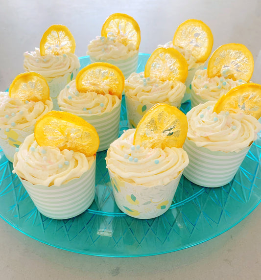 homemade lemon cupcakes with swirly piped frosting and candied lemon decoration. cupcakes are arranged on a transparent teal plate that is setting on a gray countertop