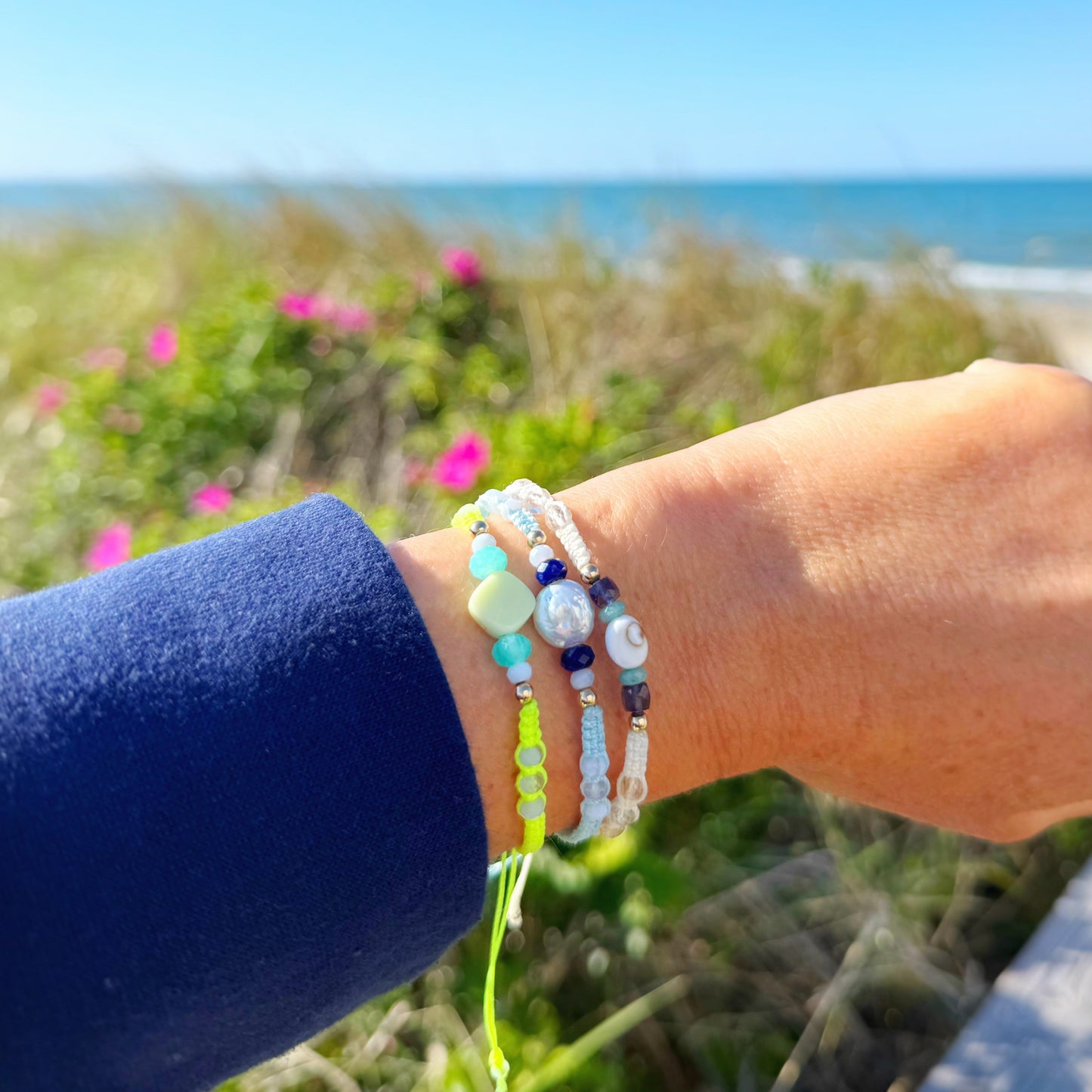 Hand wearing multiple bracelets with a scenic background of ocean and sky.