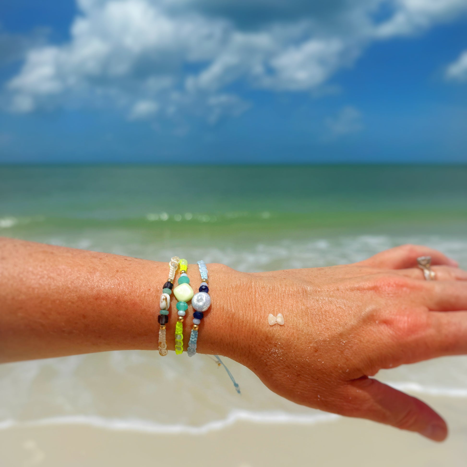 Hand with colorful bracelets on a beach with ocean and sky in the background