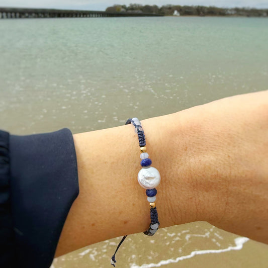 Person wearing a navy blue macrame bracelet with a scenic view of water and sky in the background