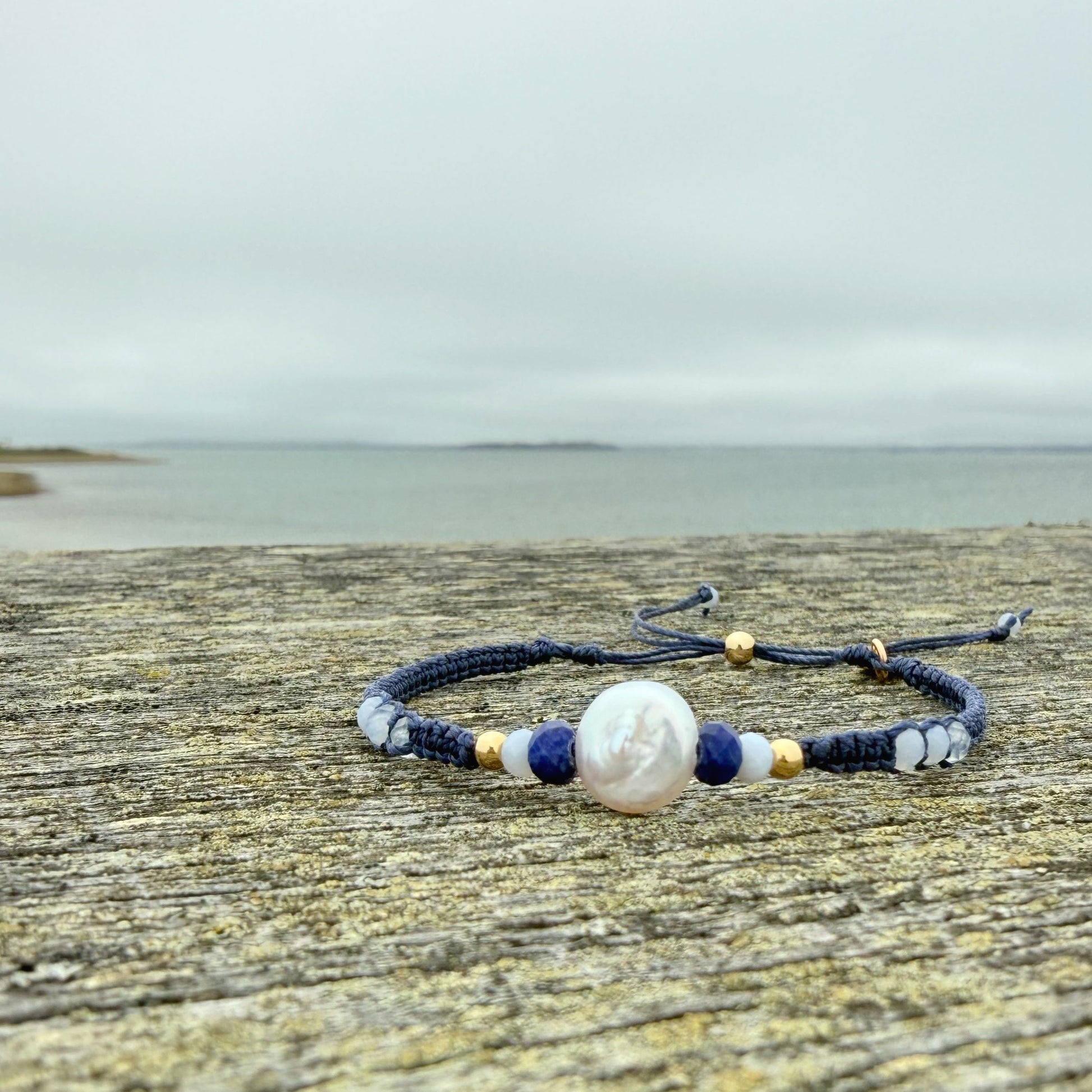 Navy blue macrame Bracelet with a pearl bead on a wooden surface with a beach background