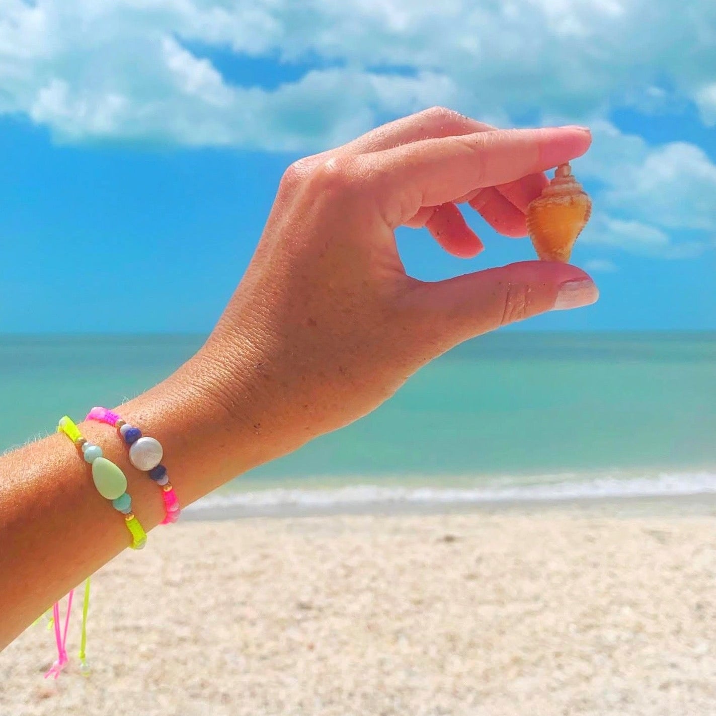 Hand holding a small shell with colorful bracelets on a beach