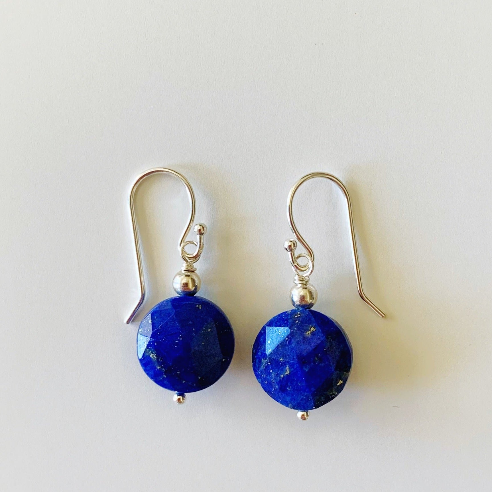 the cobalt sky earrings by mermaids and madeleines are designed with lapis faceted coin beads. Its a traditional small drop earring style with sterling silver bead and findings. this pair is photographed flat on a white surface