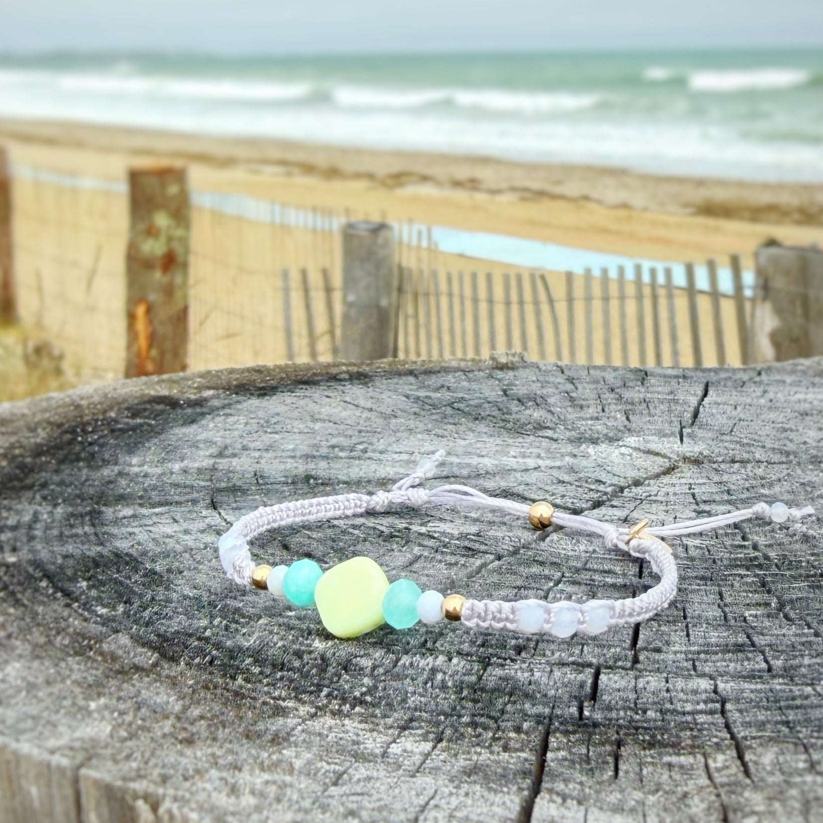 Light purple macrame Bracelet with a lime green bead at the center on a wooden post by the beach