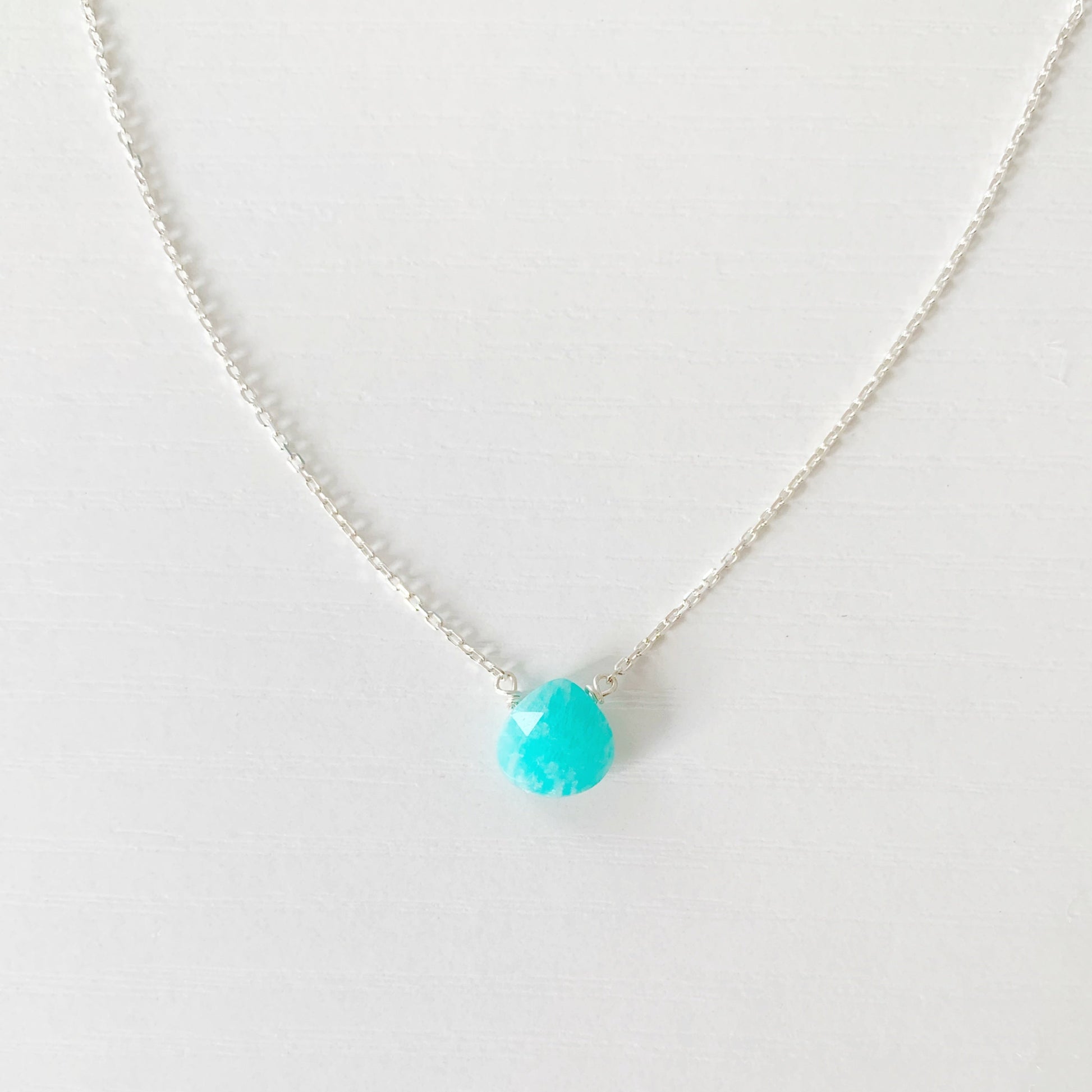 the captiva necklace by mermaids and madeleines is a dainty drop necklace featuring a small, faceted, bright teal amazonite briolette, on 17" sterling silver lightweight chain. This necklace is photographed close up on a white surface