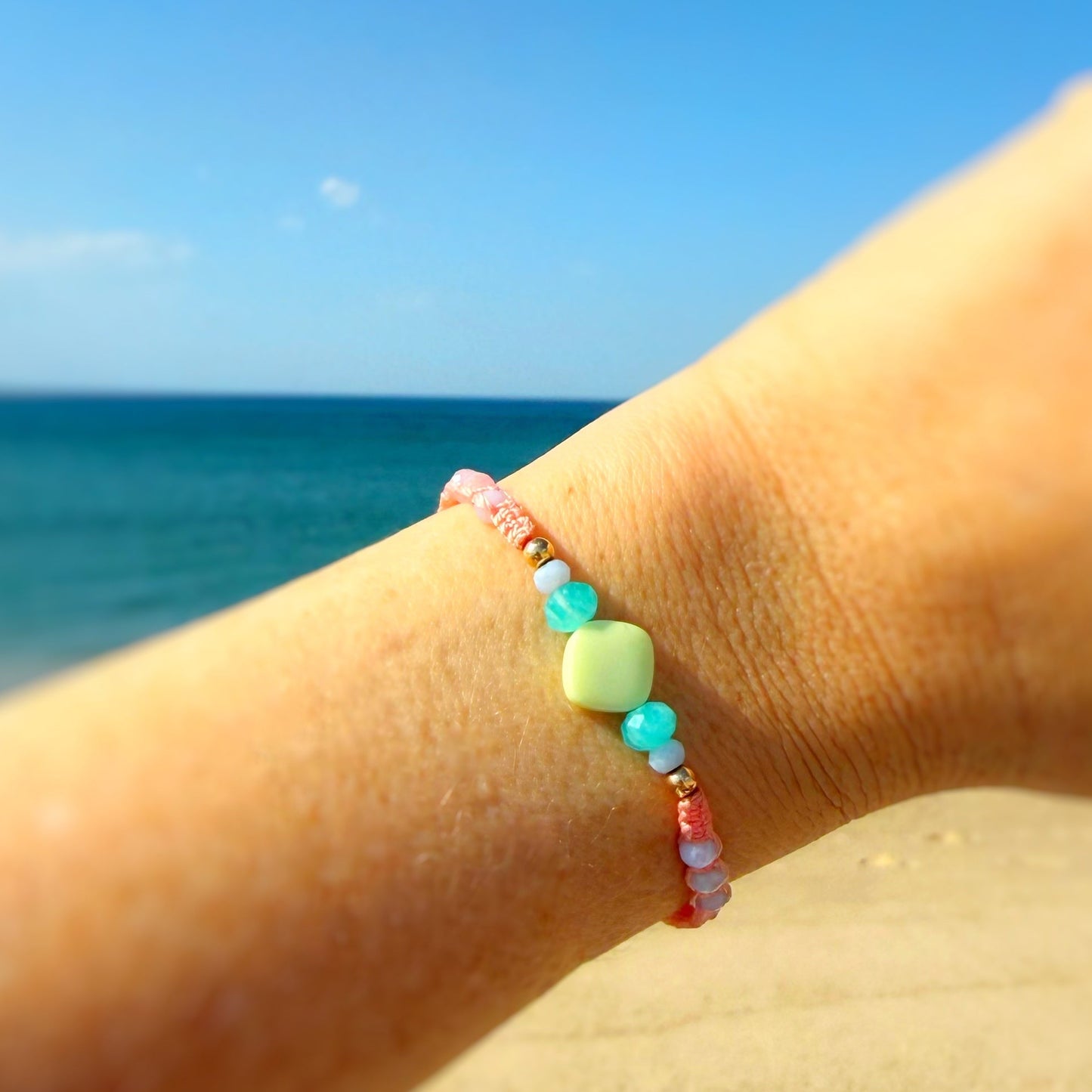 Close-up of a wrist wearing a colorful woven bracelet with beads at the center with a beach and ocean background.