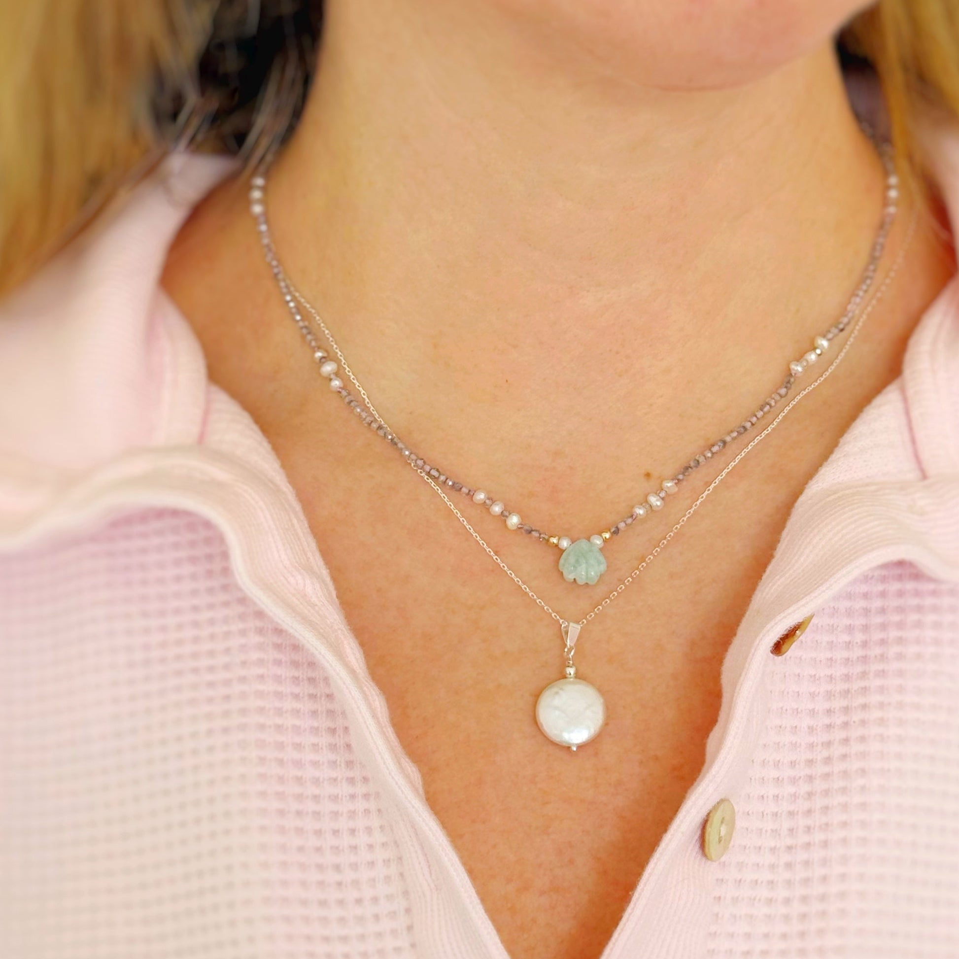 Necklaces layered, a small beaded necklace worn with a pearl pendant worn by a person in a pink shirt